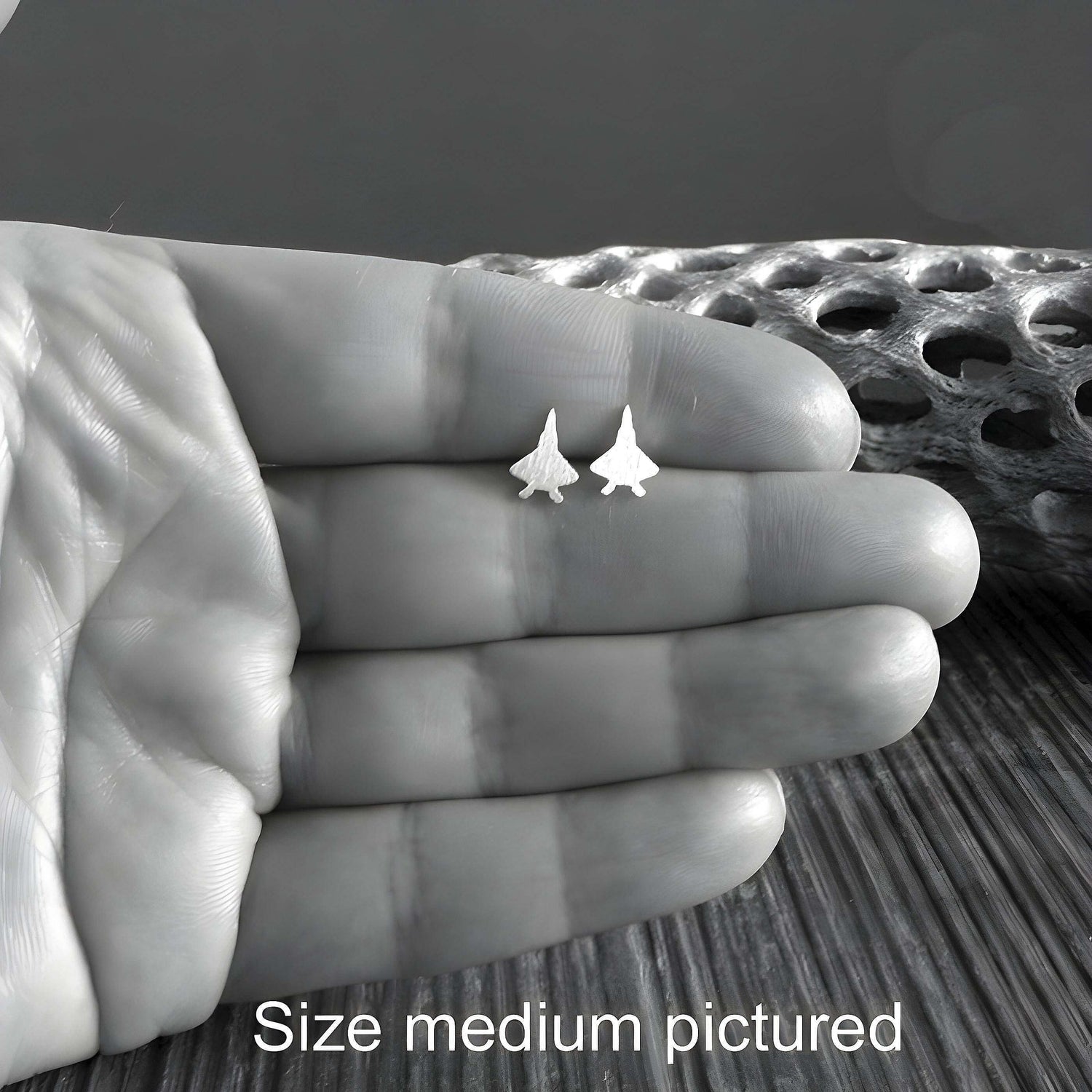 Pair of F-22 Raptor Fighter Jet silver stud earrings held in a hand close up
