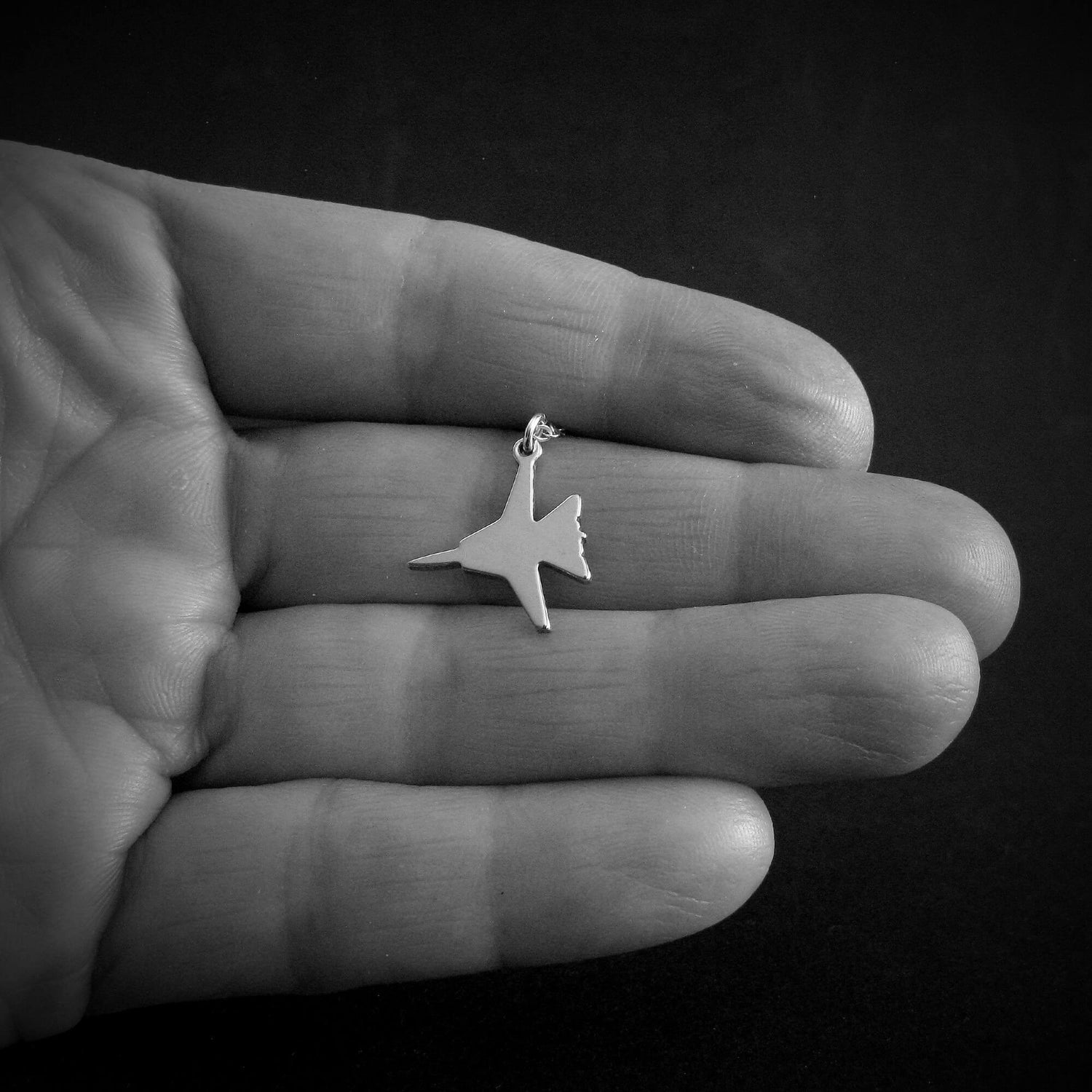 Hand holding small sterling silver F-14 Tomcat pendant necklace, handcrafted fighter jet jewelry for pilots