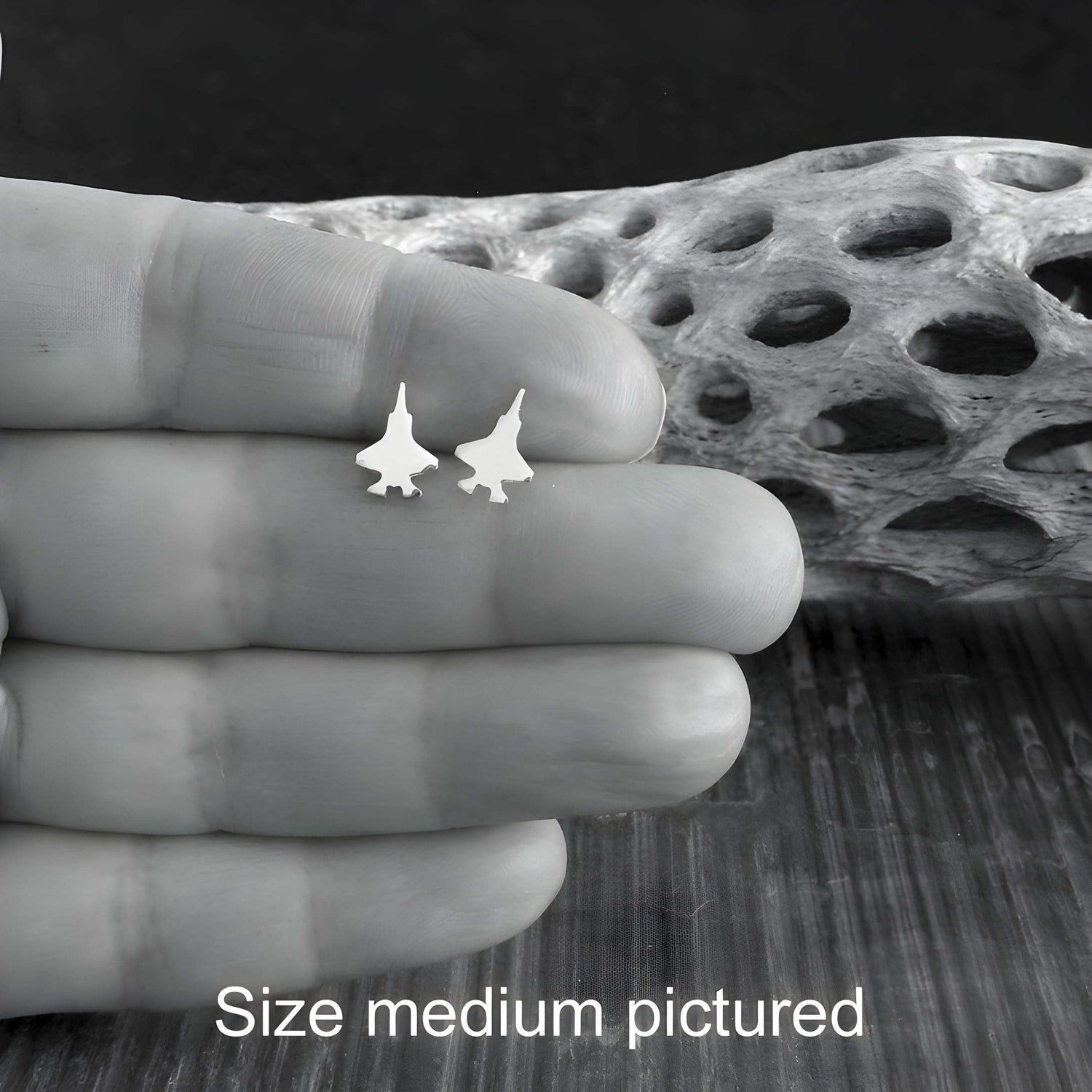 Small F-35 Jet airplane shaped earrings held between fingers with a textured background