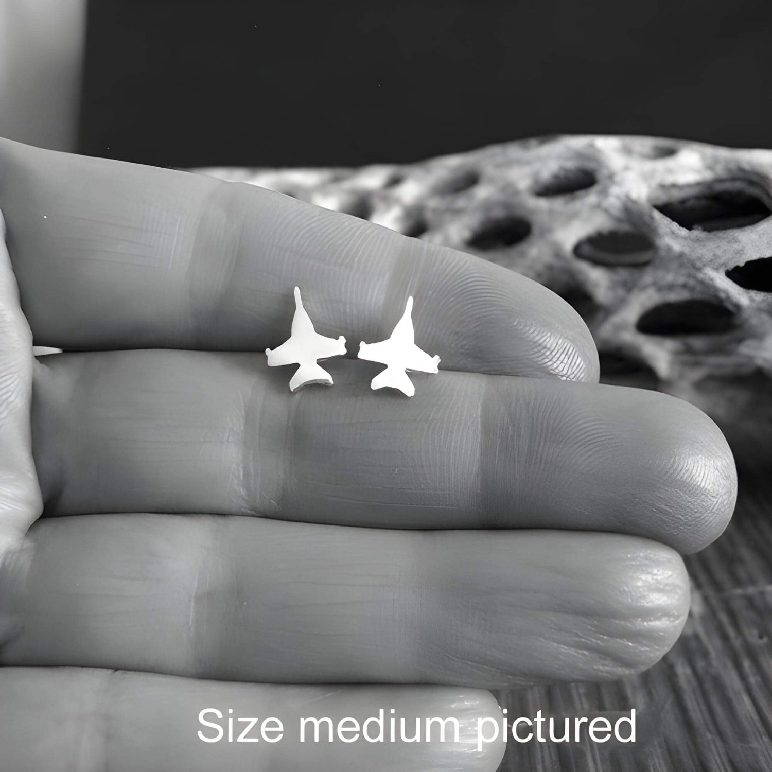 Pair of sterling silver F-18 Hornet Jet Fighter stud earrings held in a hand between fingers close up
