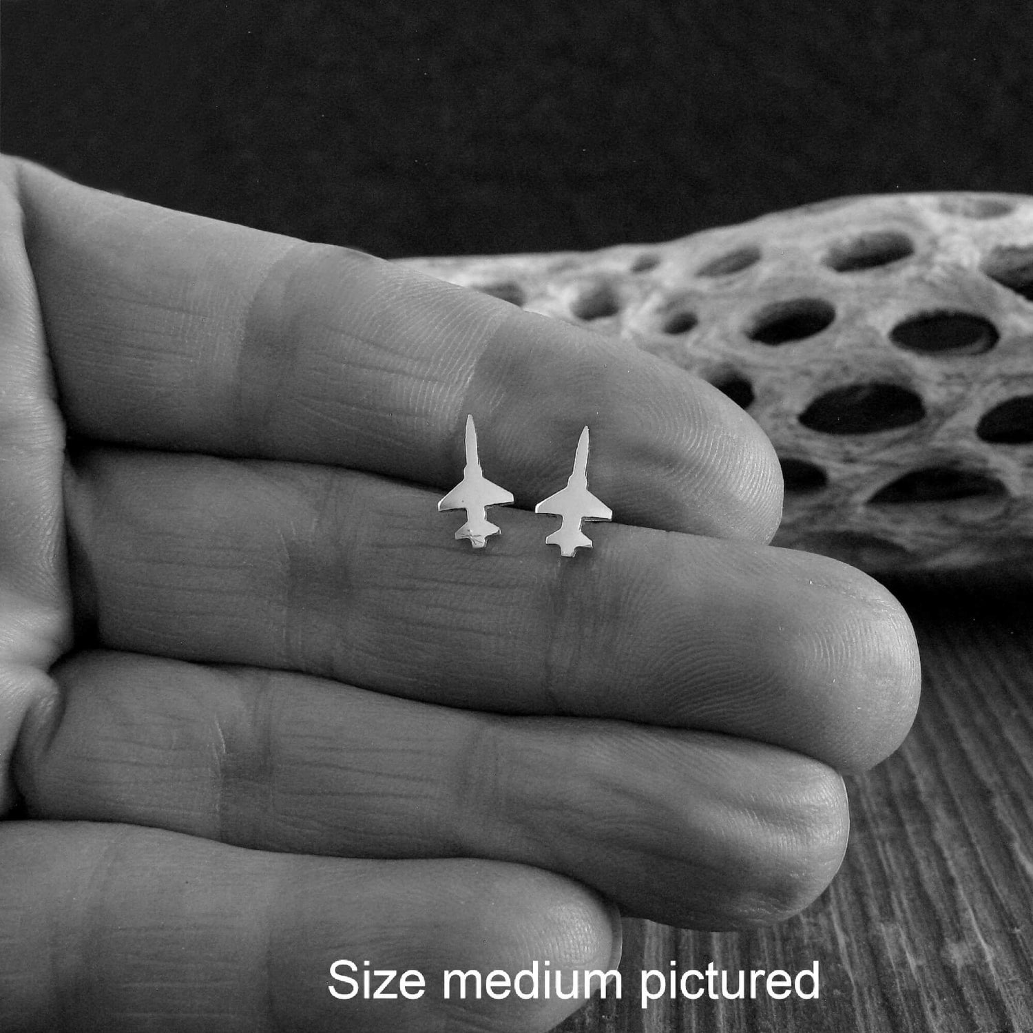 Pair of sterling silver F-5 Fighter Jet Stud Earrings in a hand close up with driftwood in the background