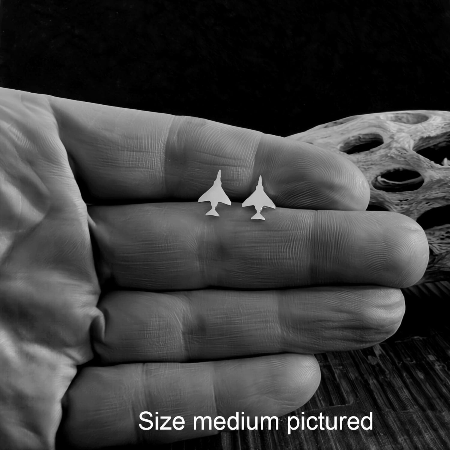 Close up view of sterling silver F-4 fighter jet stud earrings held in a hand between the fingers
