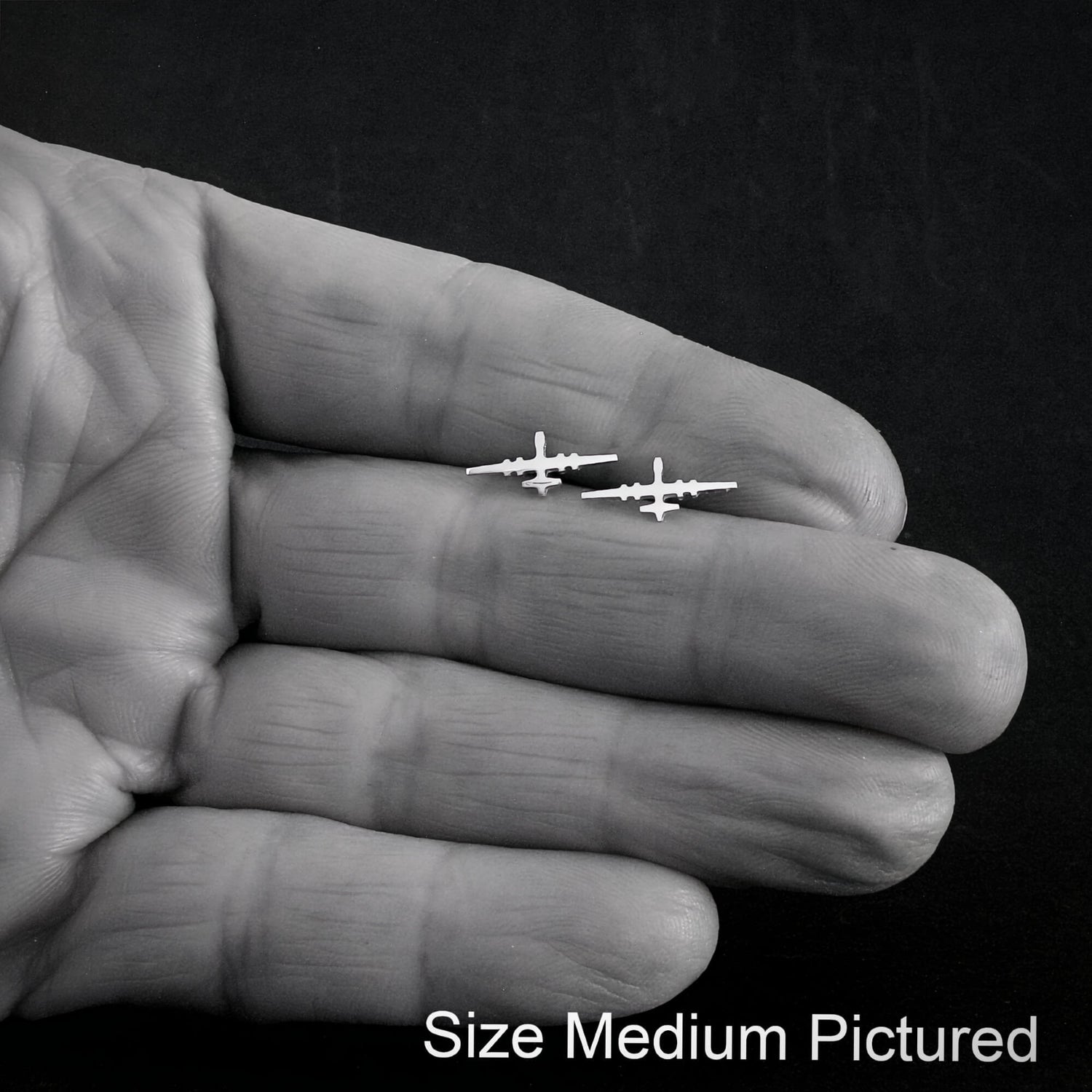 Small MQ-9 Reaper Military Drone earrings held between fingers against a dark background
