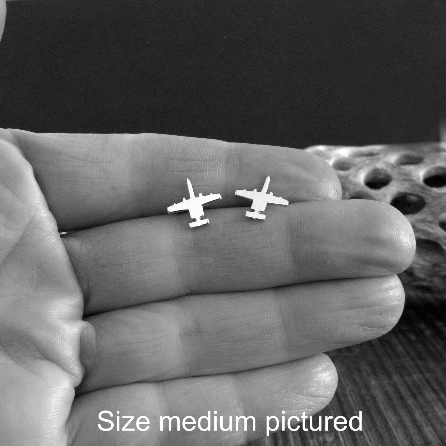 A hand holding a small pair of sterling silver A-10 Warthog Jet Airplanes on a dark background