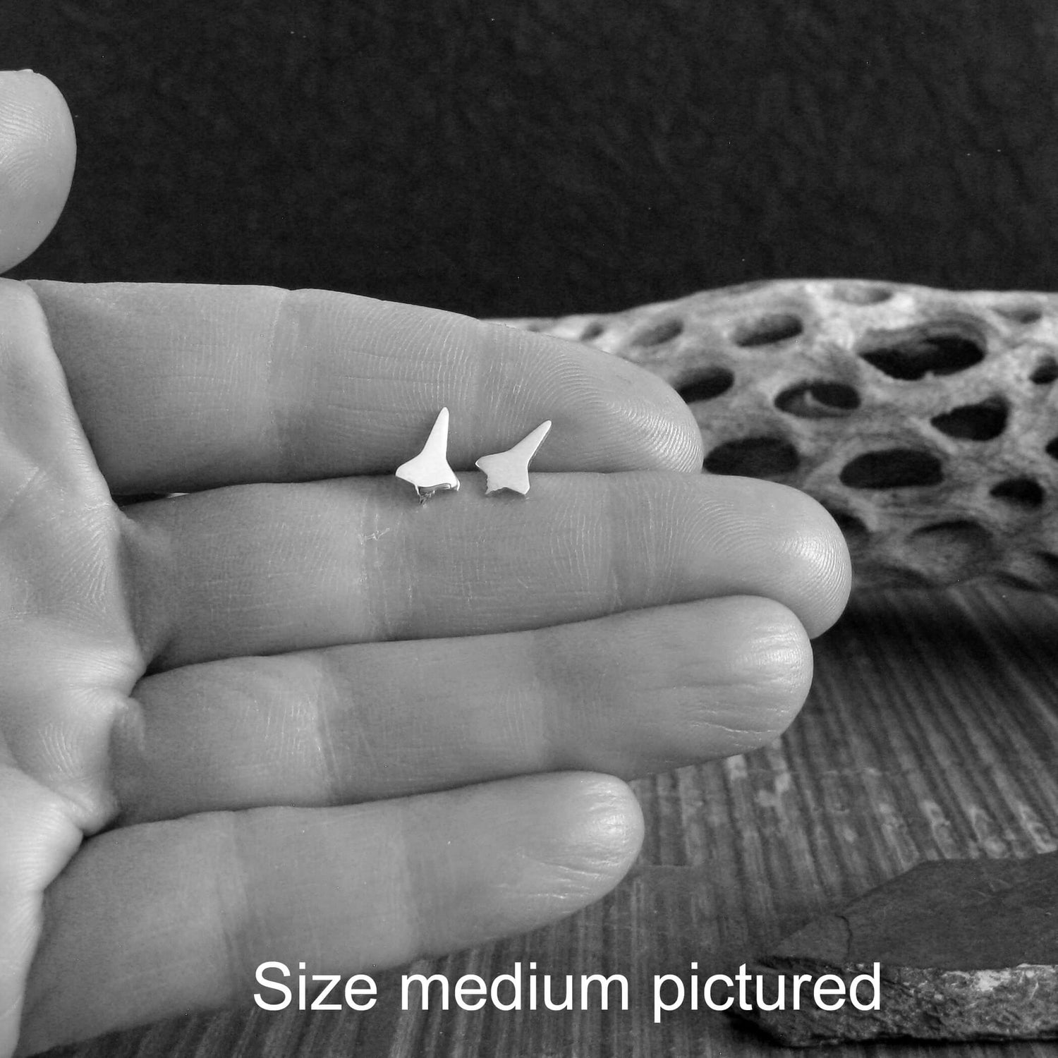 Pair of sterling silver NASA Space Shuttle stud earrings held in a hand between fingers close up