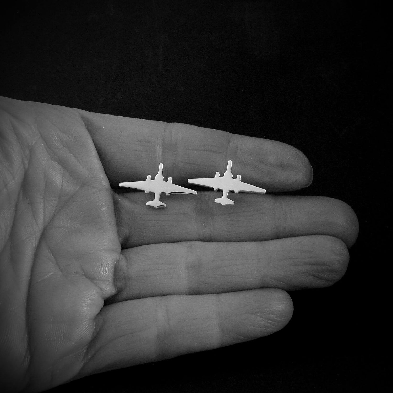 Two small U-2 Dragon Lady Military airplane cufflinks held in a hand against a black background
