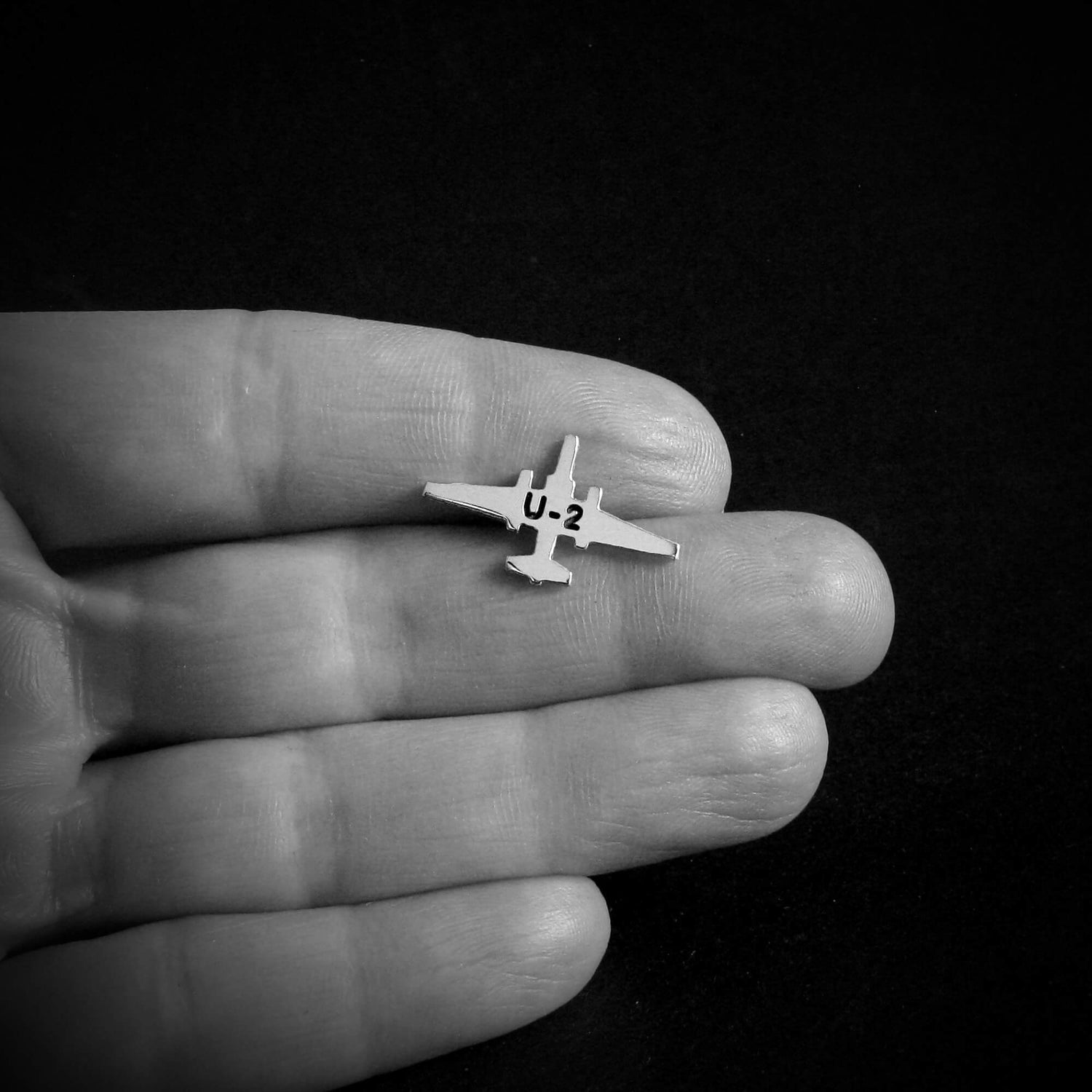 Small U-2 Dragon Lady Military Jet airplane tie tack held between fingers against a black background