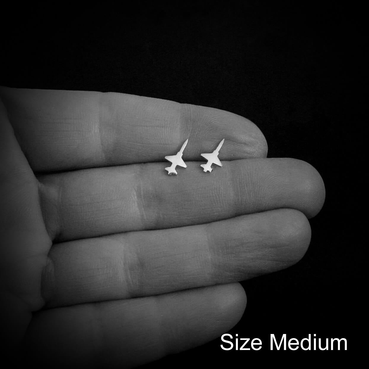 Small T-38 airplane-shaped earrings held in a hand against a black background