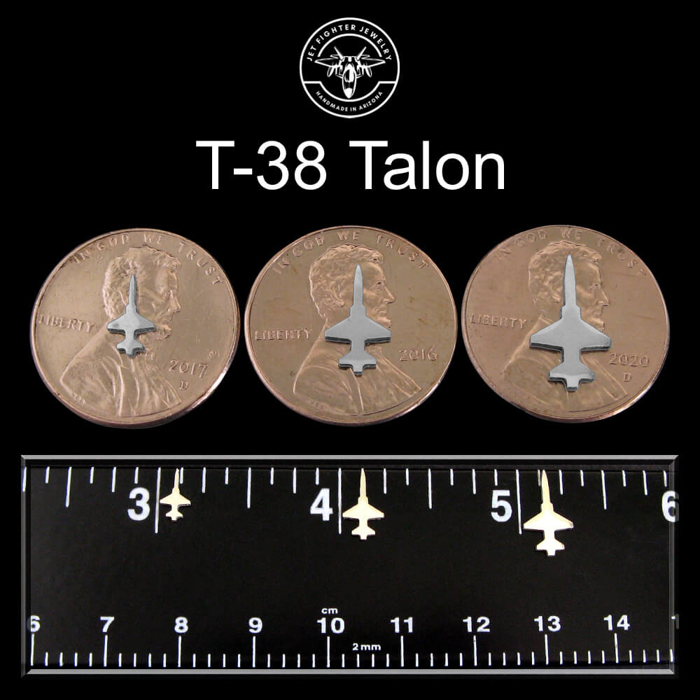 Three T-38 Talon airplane designs on pennies on a black background with a ruler for scale.