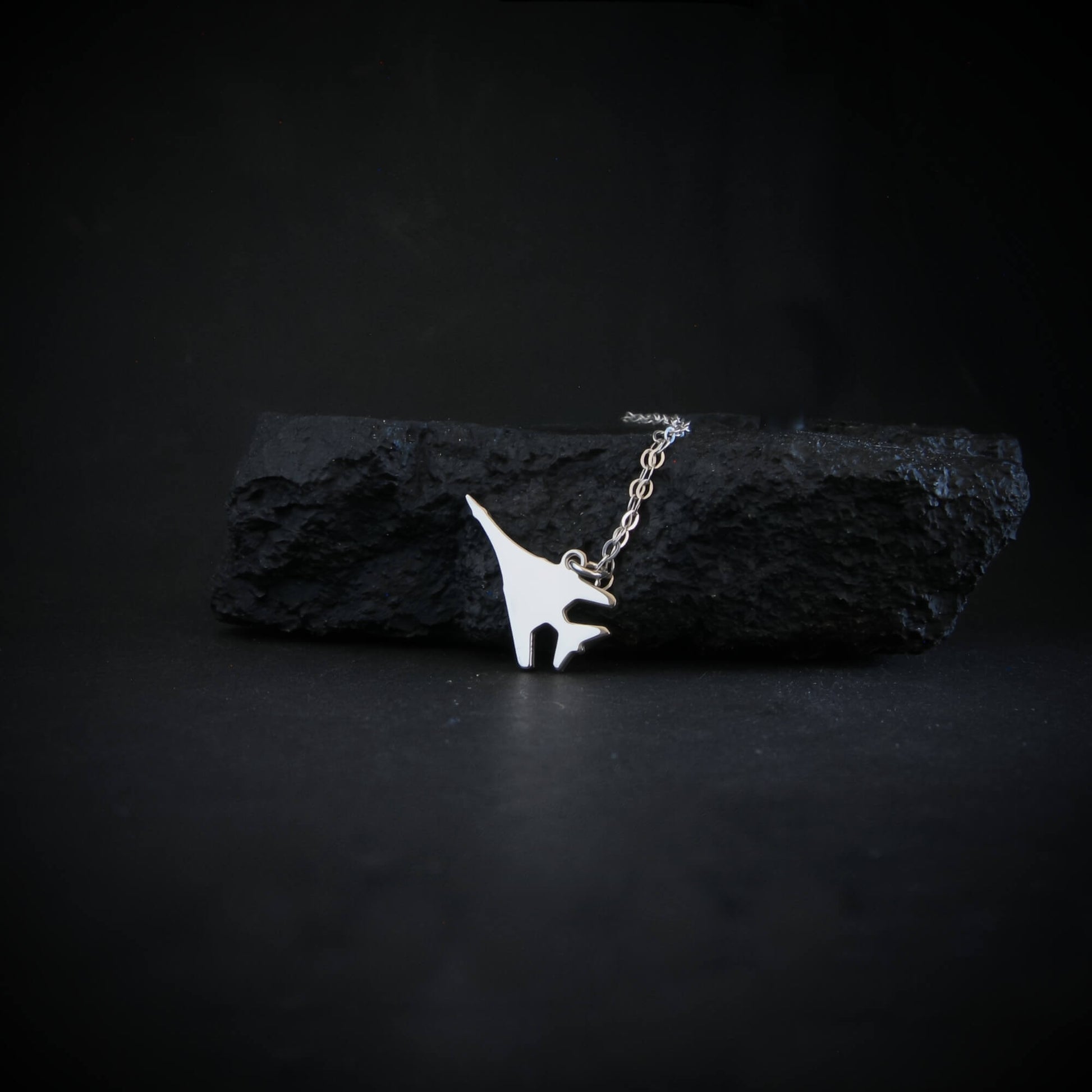 Sterling silver B-1 Lancer bomber pendant necklace resting on black rock – artisan aviation jewelry handmade in USA