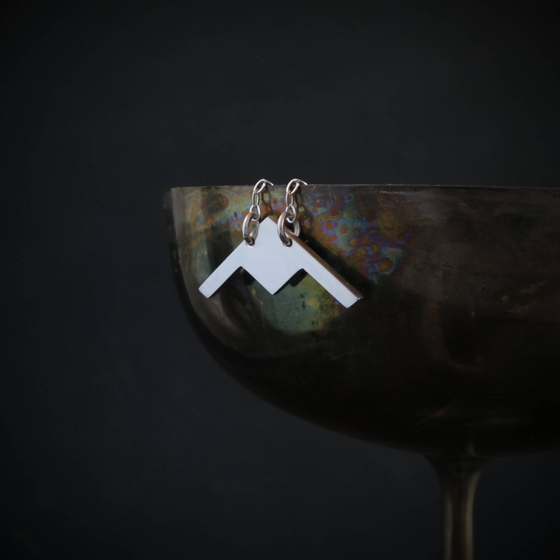 Handmade sterling silver B-21 Raider bomber jet pendant displayed on metallic goblet