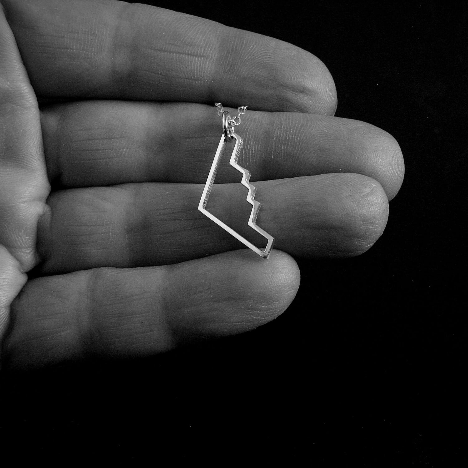 Silver B-2 Bomber Military Jet airplane outline pendant necklace held in a hand against a black background