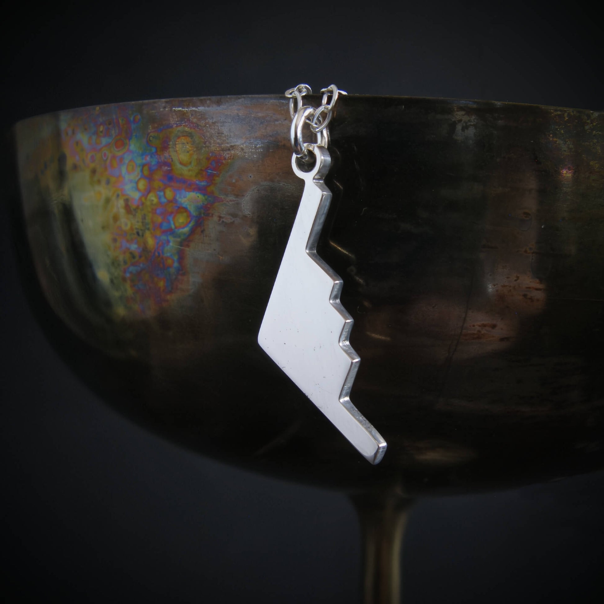 Silver B-2 Spirit Bomber Military Jet necklace pendant hanging from a reflective surface
