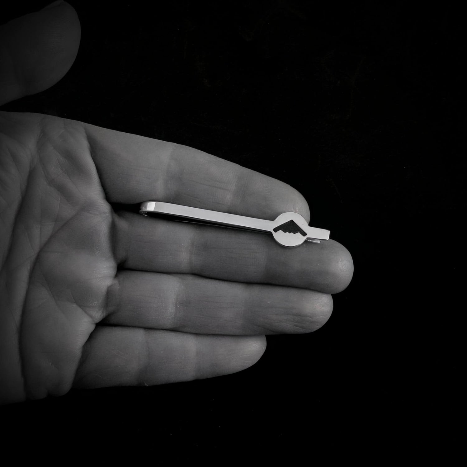 Sterling silver B-2 Spirit Bomber tie clip with engraved silhouette shown resting in hand for scale