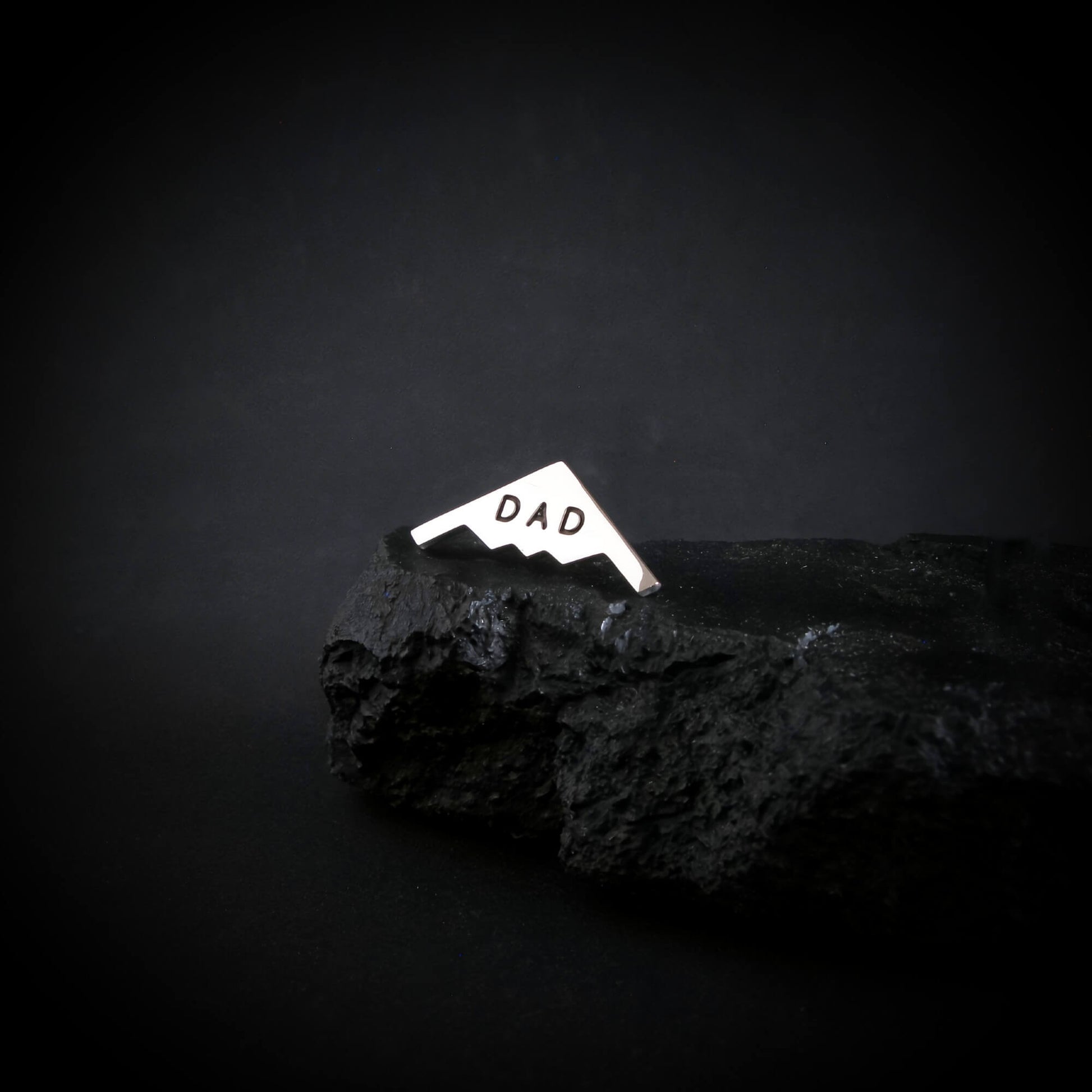 Sterling silver B-2 bomber tie tack engraved with "DAD" displayed on rugged black stone, handmade military aviation jewelry for Father's Day or pilot gifts