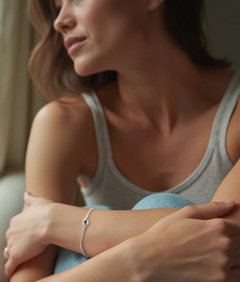 Woman sitting with her arms around her knees wearing a dainty bracelet with an engraved B-2 bomber jet fighter