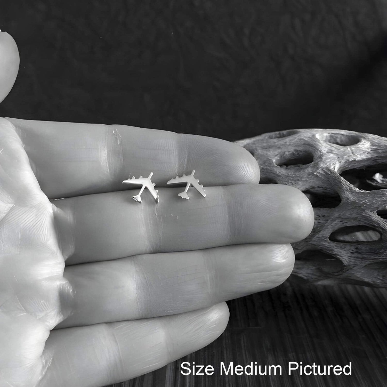 Small B-52 Military Jet airplane earrings held between fingers with a dark background