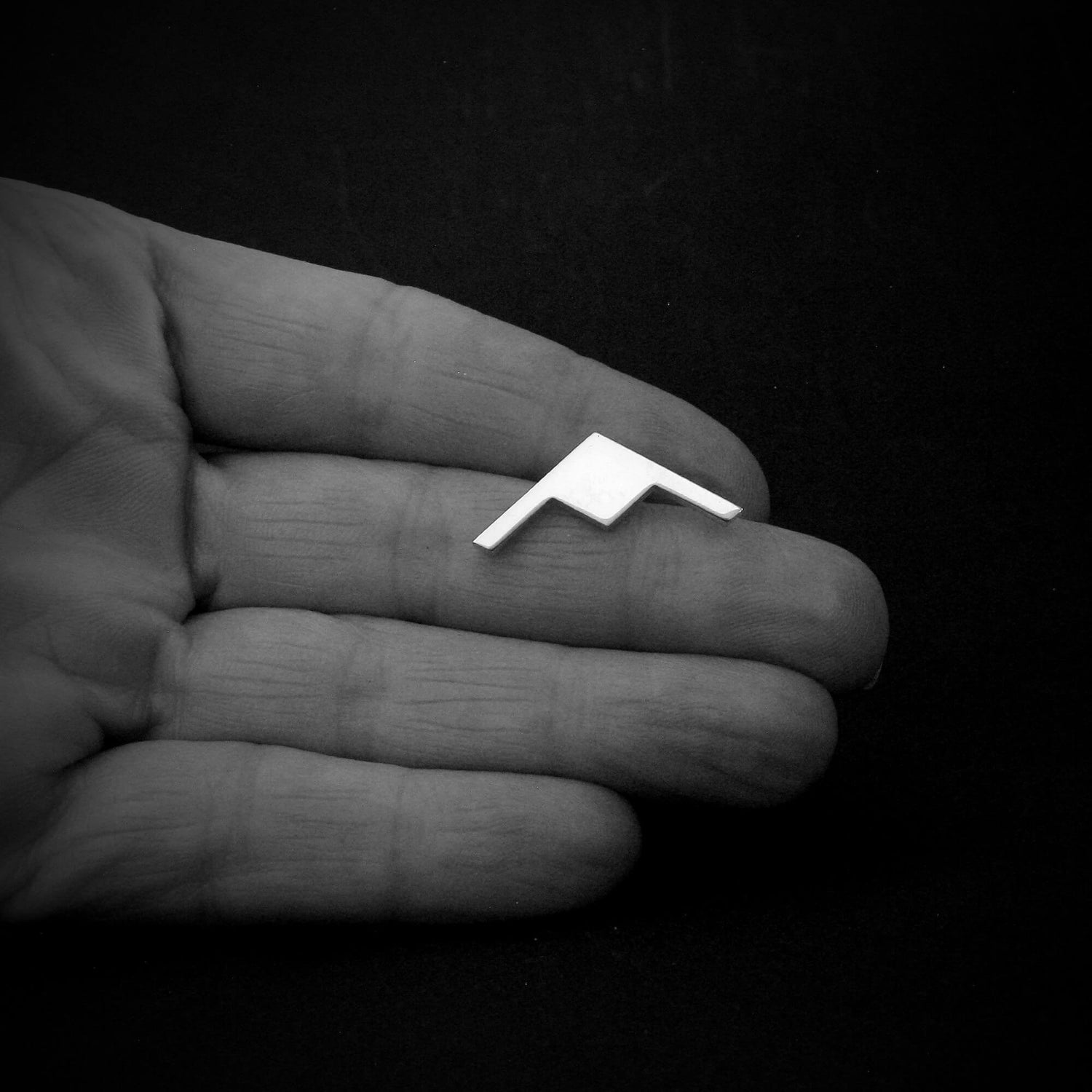 Silver B-21 Raider Bomber Military Jet Tie Pin held in a hand against a black background