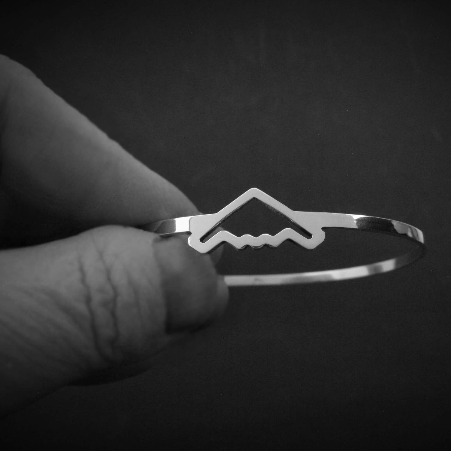 B-2 Bomber Jet Silver bangle bracelet held by a hand against a dark background