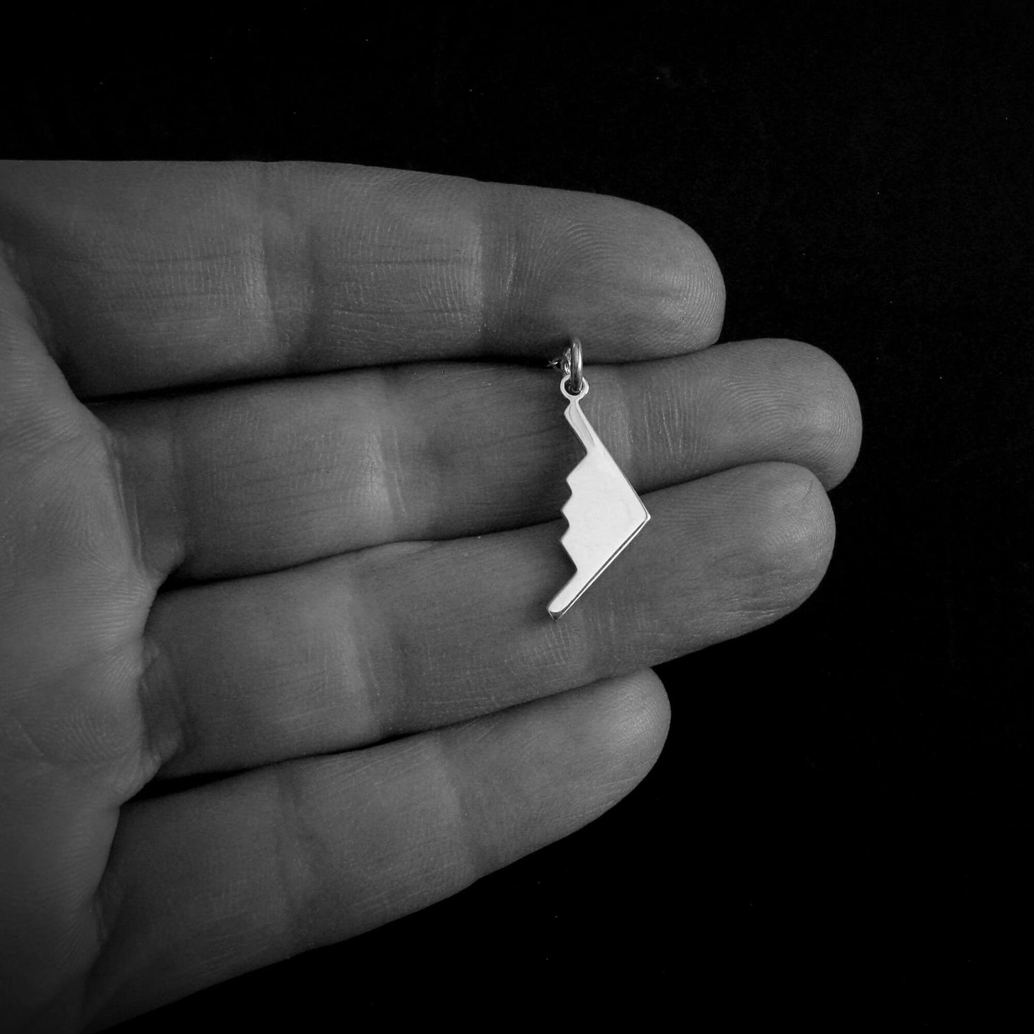 Silver jewelry B-2 Spirit Stealth Bomber Military jet Fighter Pendant necklace on a hand against a black background