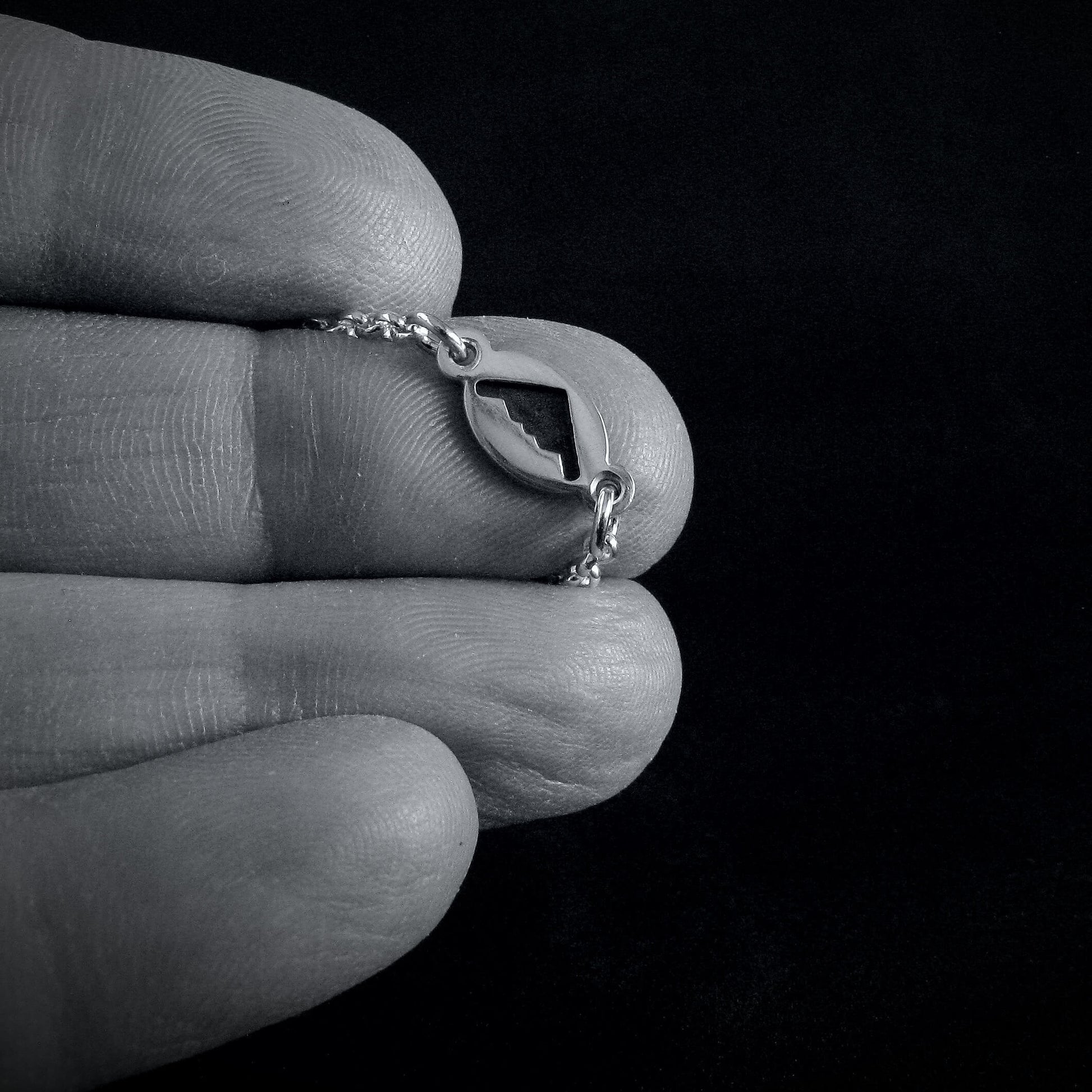 Close-up of a hand holding a delicate  B-2 jet sterling silver necklace against a black background