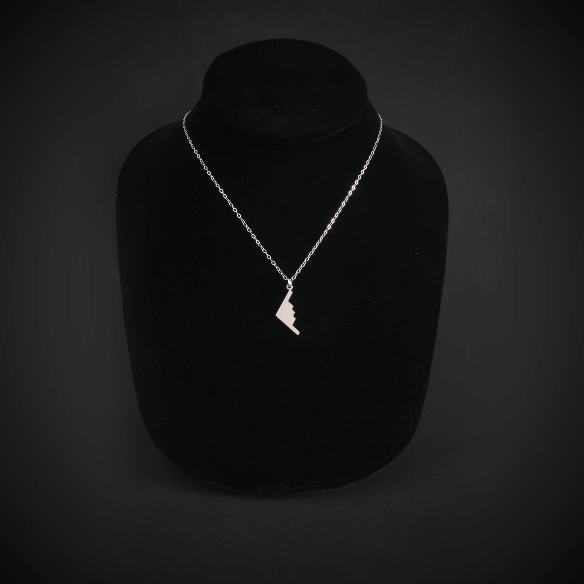 Silver B-2 Spirit Bomber Military Jet necklace with a pendant on a black mannequin against a dark background
