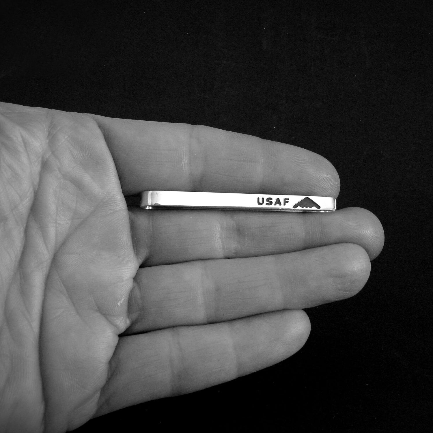 Hand holding a sterling silver tie bar with 'USAF' and B-2 Spirit silhouette engraving against a black background