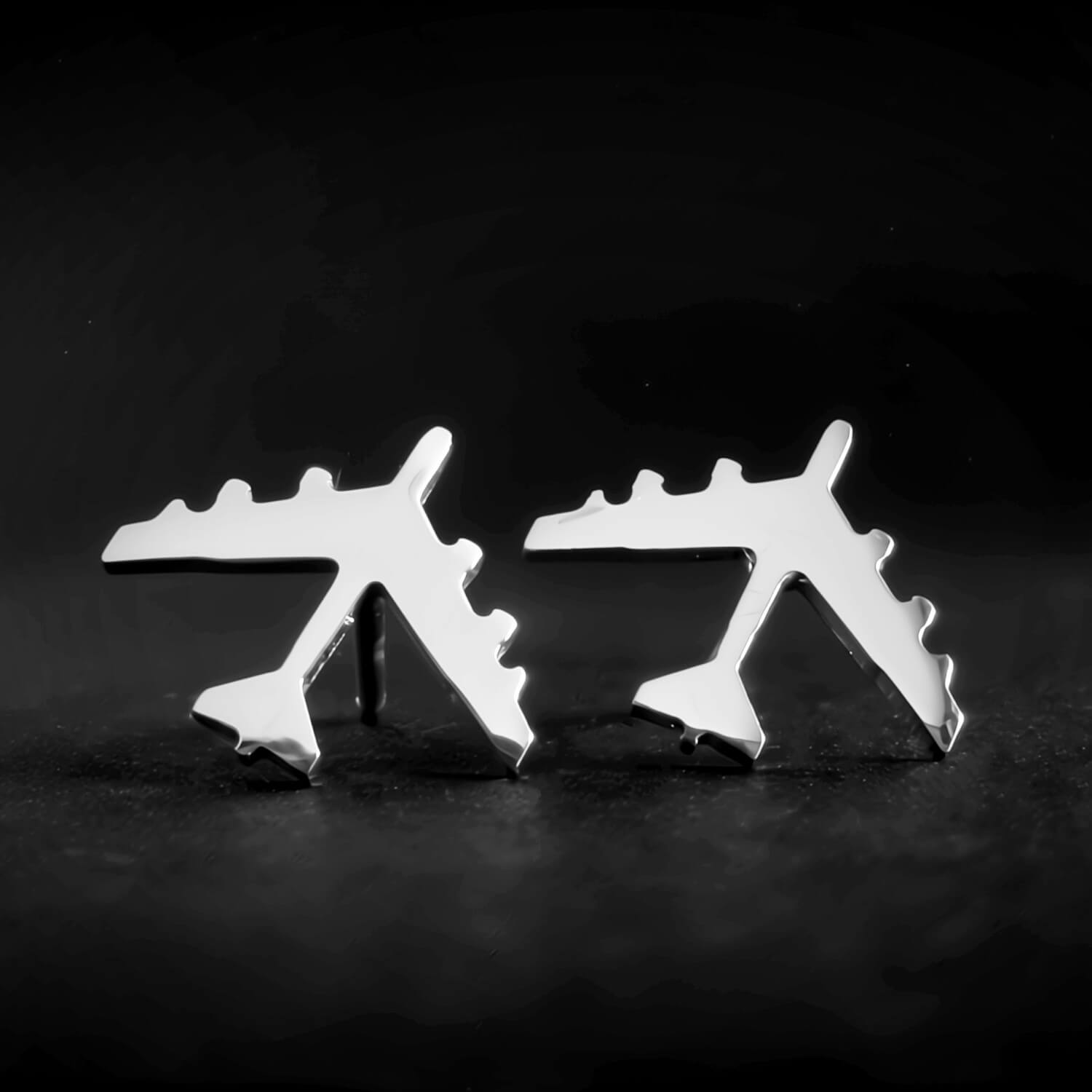 Silver B-52 military Jet airplane shaped earrings on a dark stone surface with a dark background