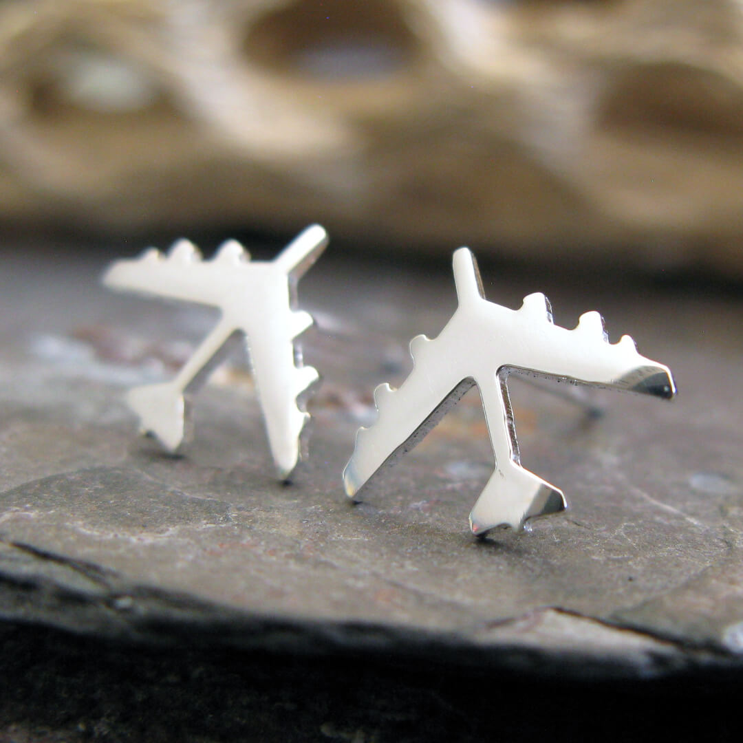 Silver B-52 military Jet airplane shaped earrings on a dark stone surface with a blurred natural background