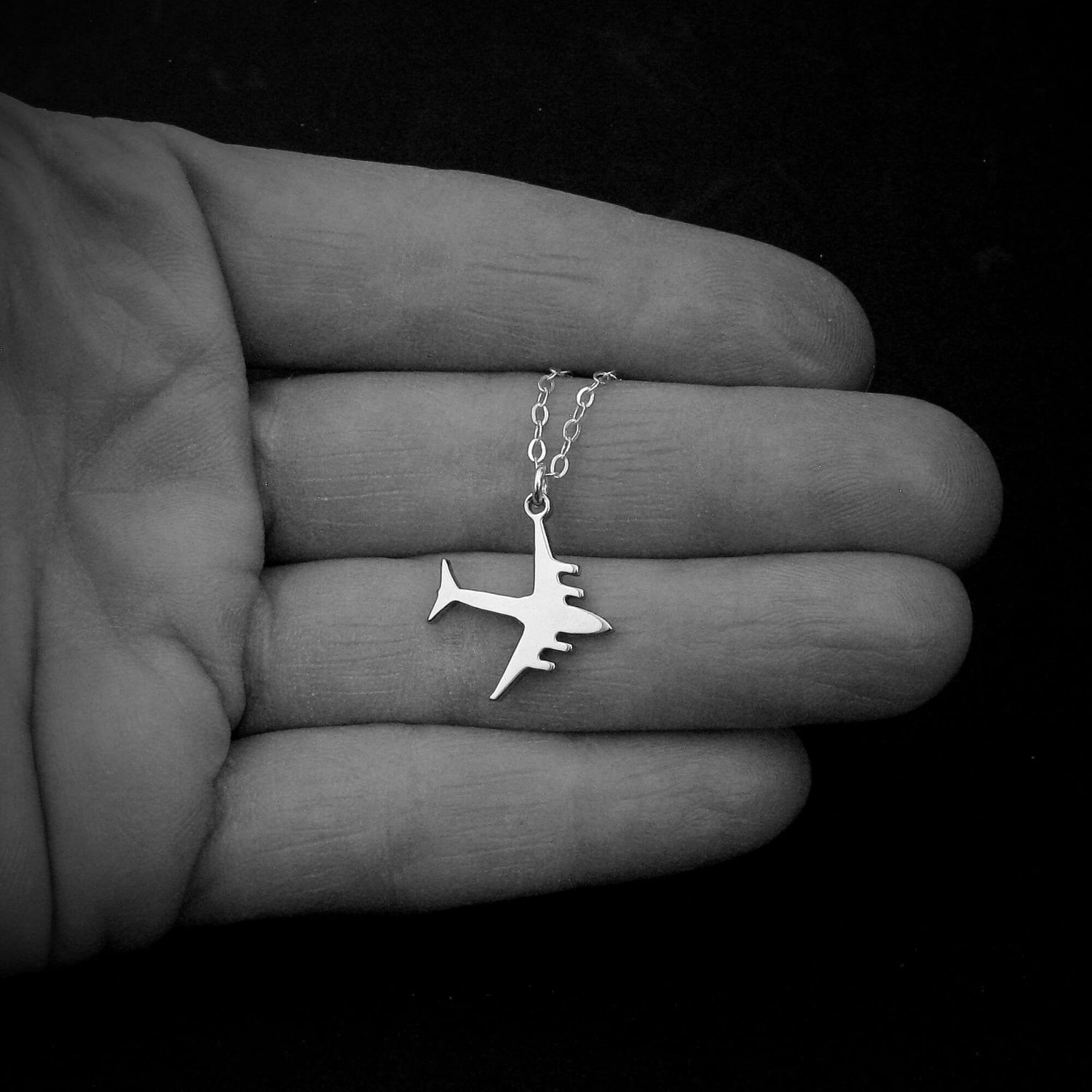 C-17 Globemaster military airplane pendant necklace in sterling silver, displayed in the palm of a hand against a black background.