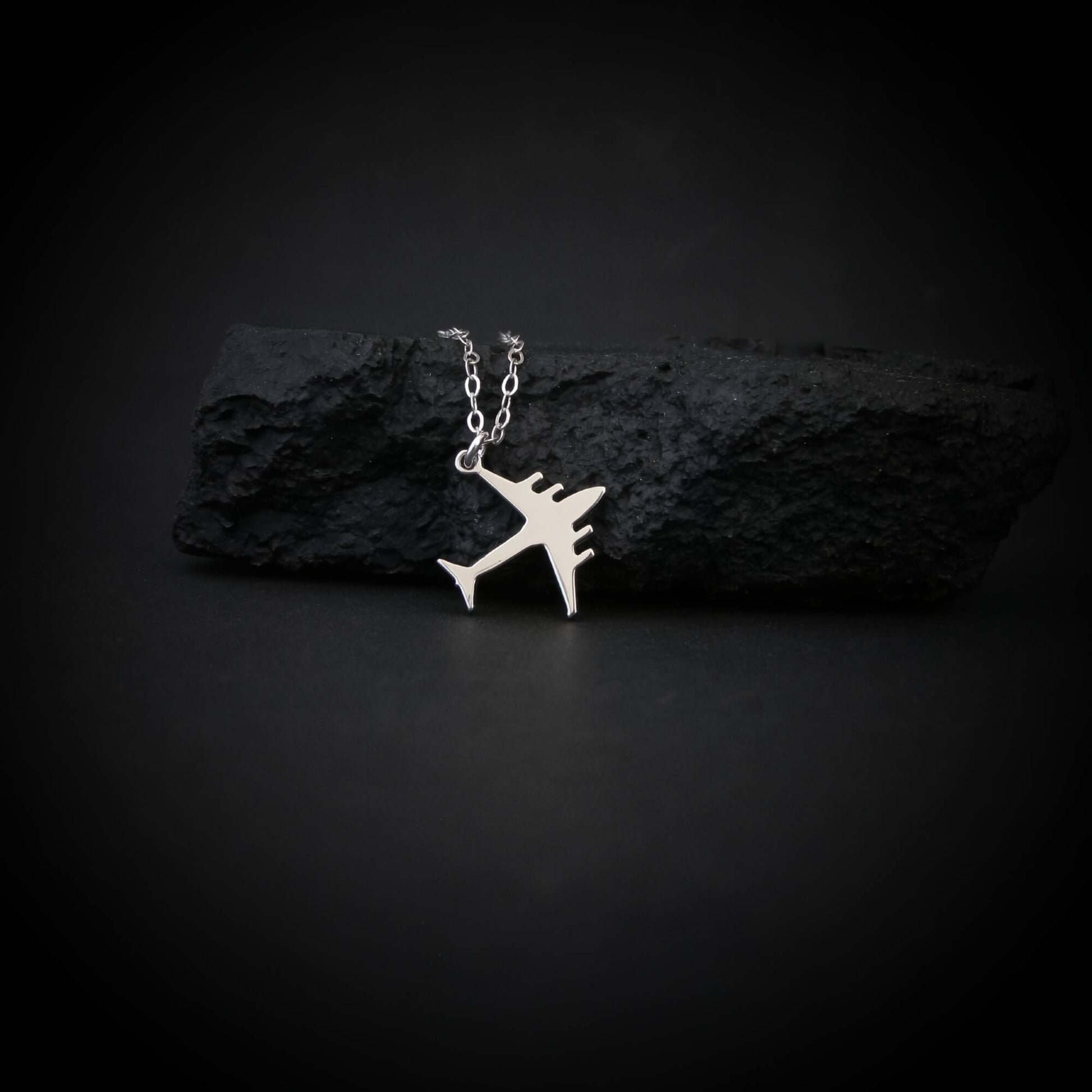 C-17 Globemaster military airplane pendant necklace in sterling silver, displayed draped over a textured black rock on a dark background.