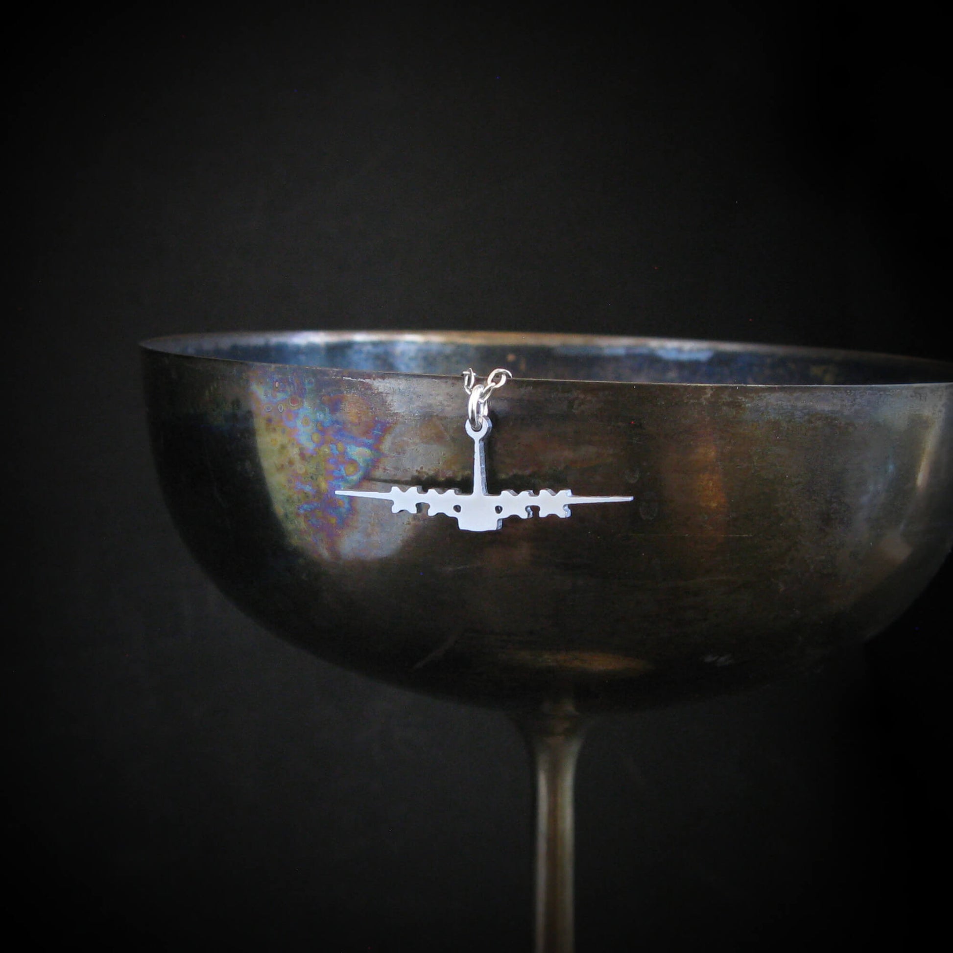 Silver C-130 necklace displayed on antique wine glass