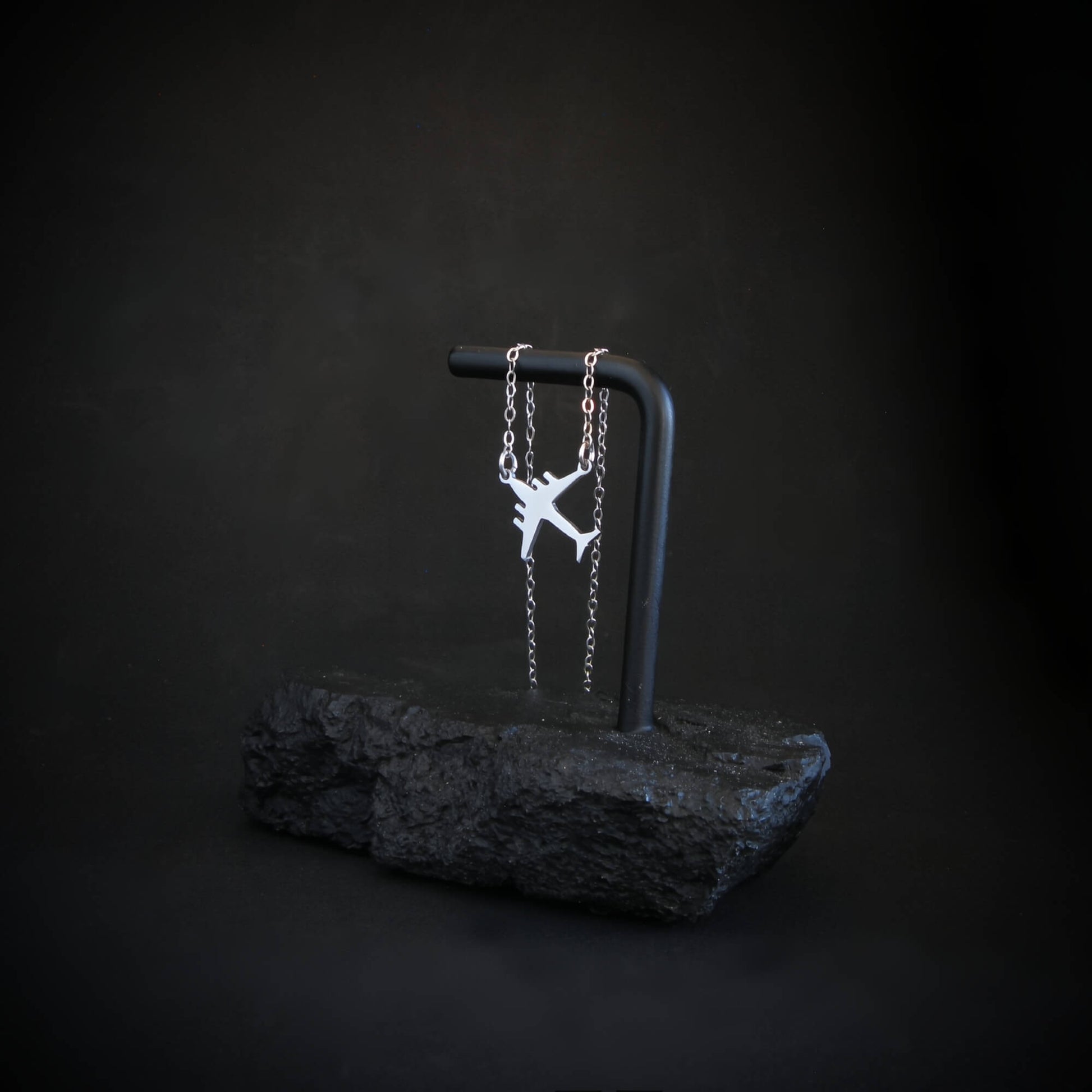 Sterling silver C-17 silhouette pendant hanging on black rock