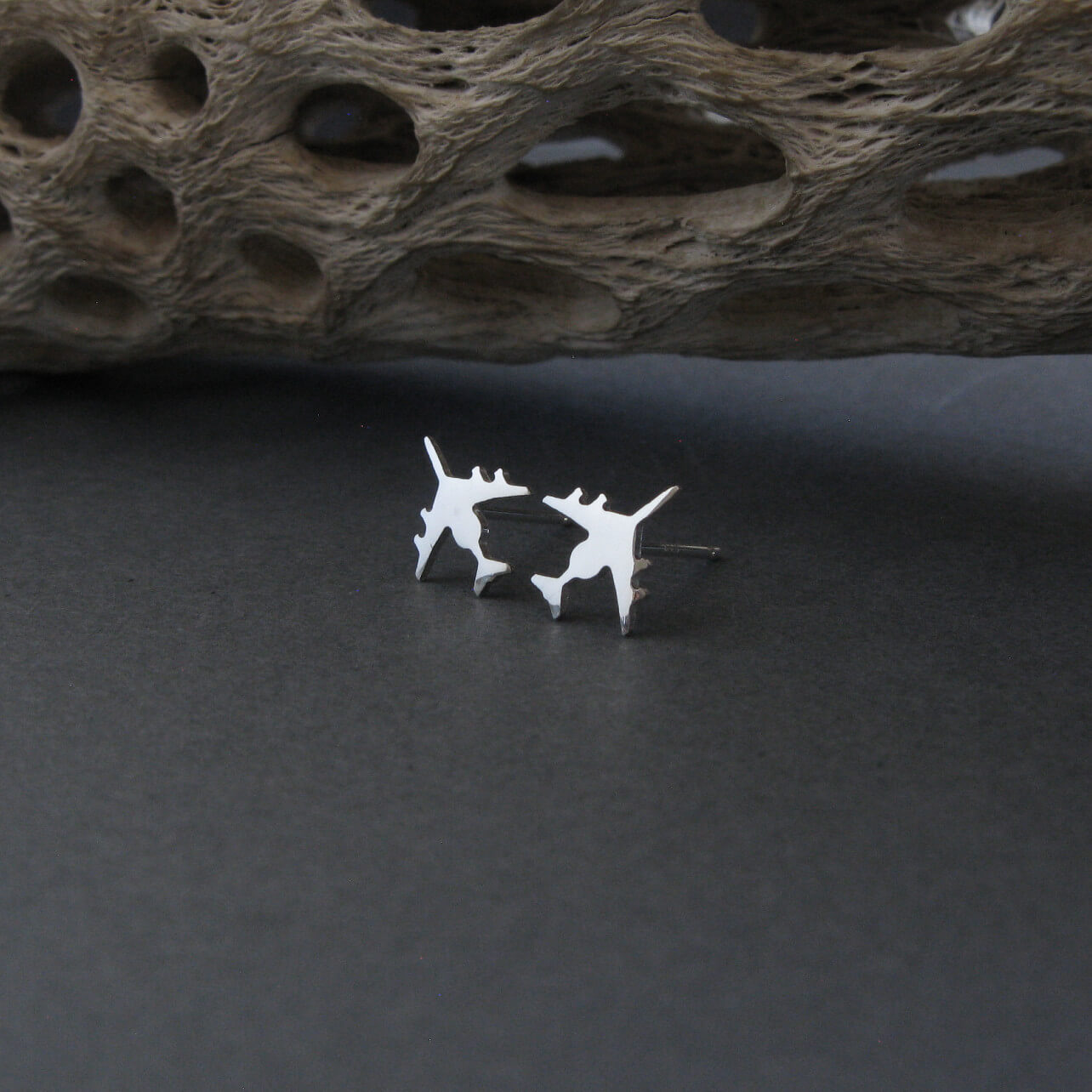 Sterling Silver E-3 Sentry military jet airplane shaped stud earrings on a dark background with driftwood