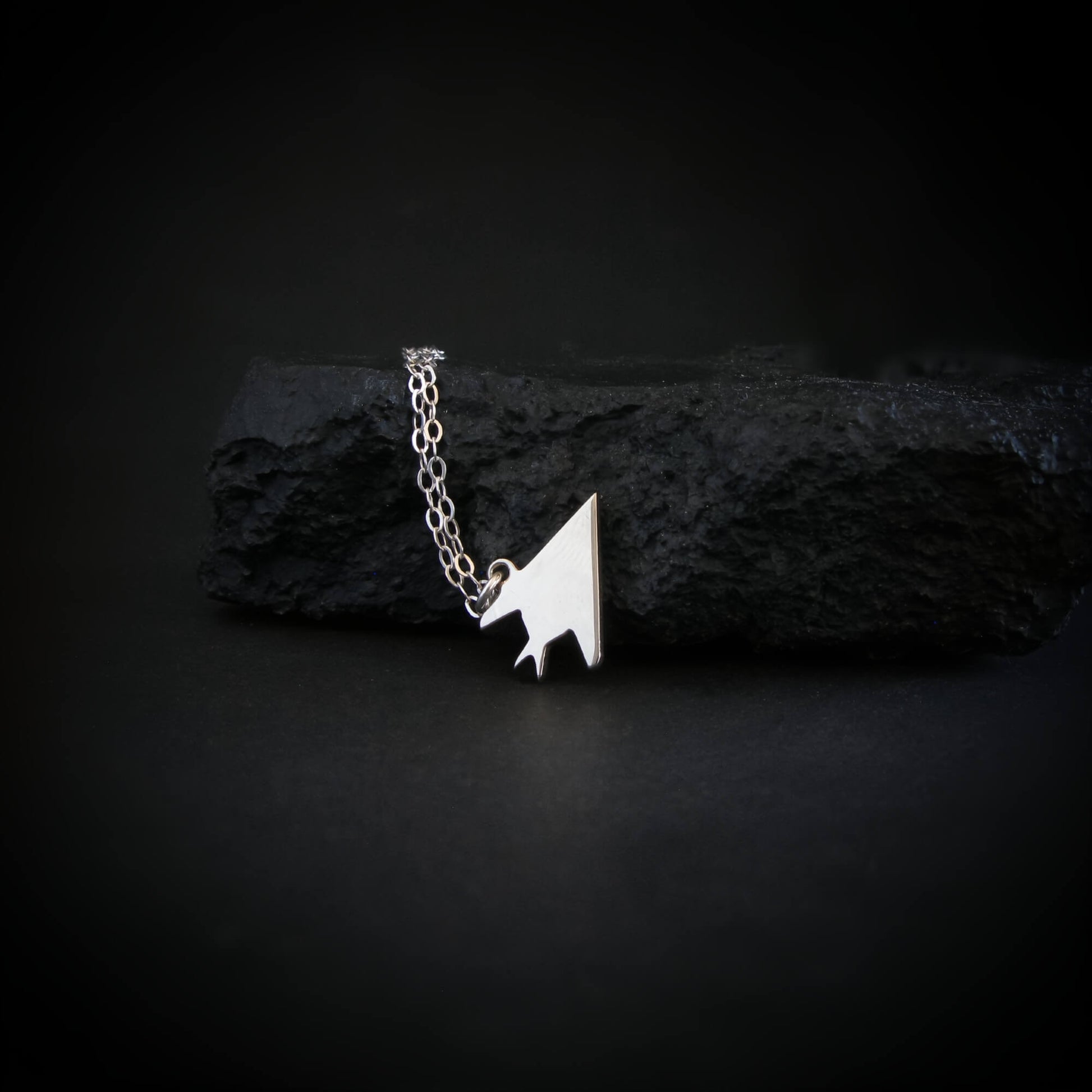 Sterling silver F-117 Nighthawk stealth jet pendant necklace resting on black rock – artisan aviation jewelry handmade in USA