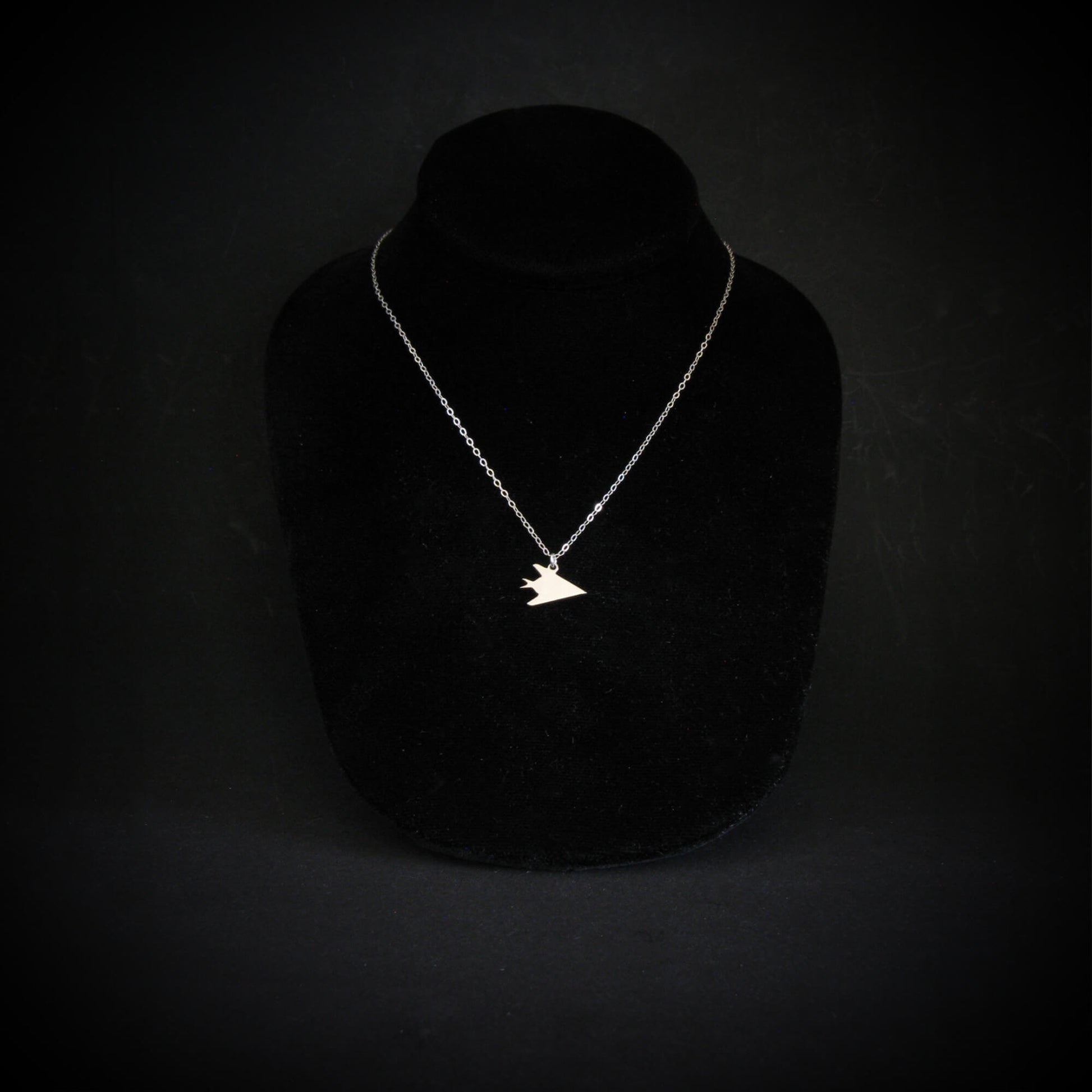 F-117 Nighthawk stealth fighter jet pendant necklace in sterling silver, handmade military aviation jewelry on black display bust
