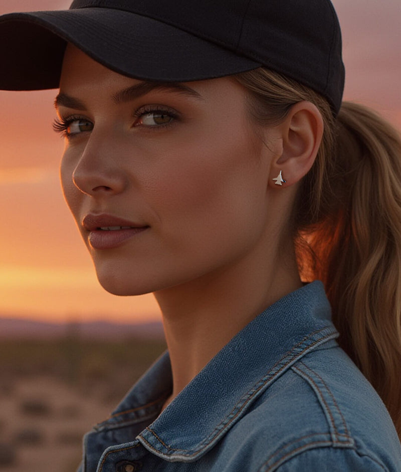 Close-up of a woman wearing F-14 jet stud earrings at sunset, styled in a denim jacket and black baseball cap—military-inspired handmade jewelry for aviation enthusiasts.