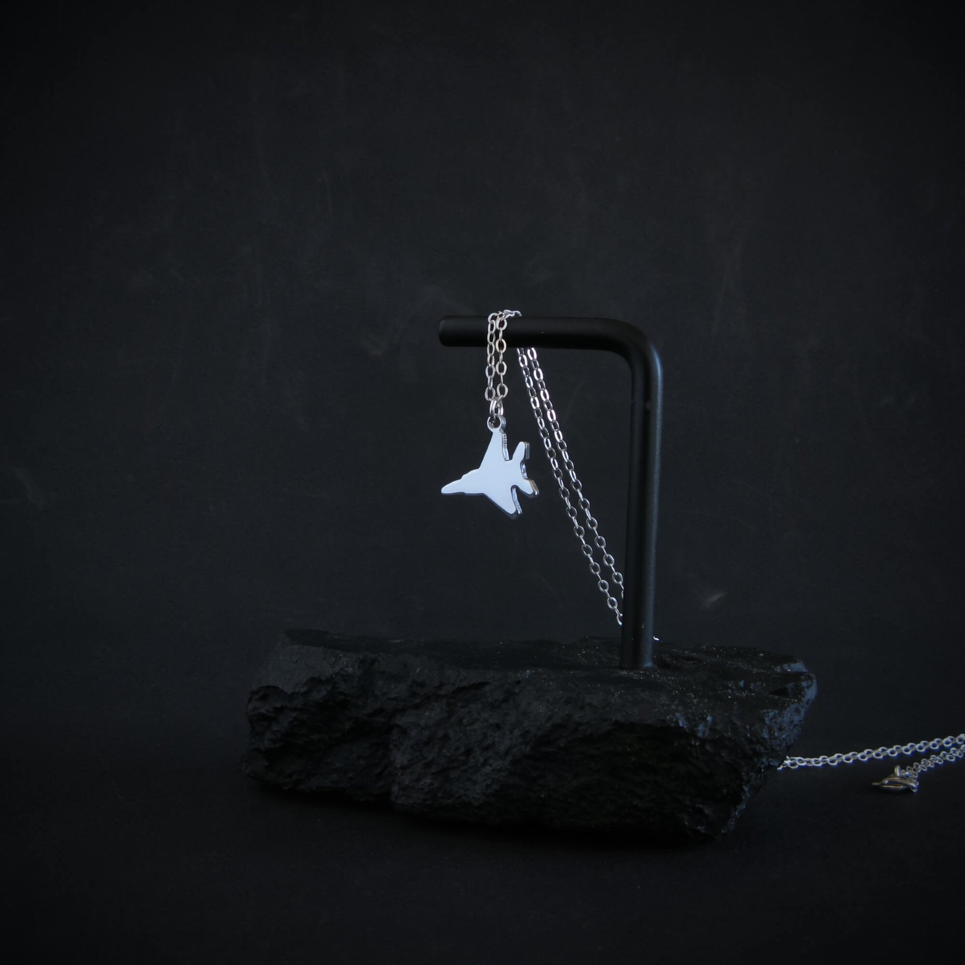 Sterling silver F-15 jet fighter necklace draped on modern black stone display