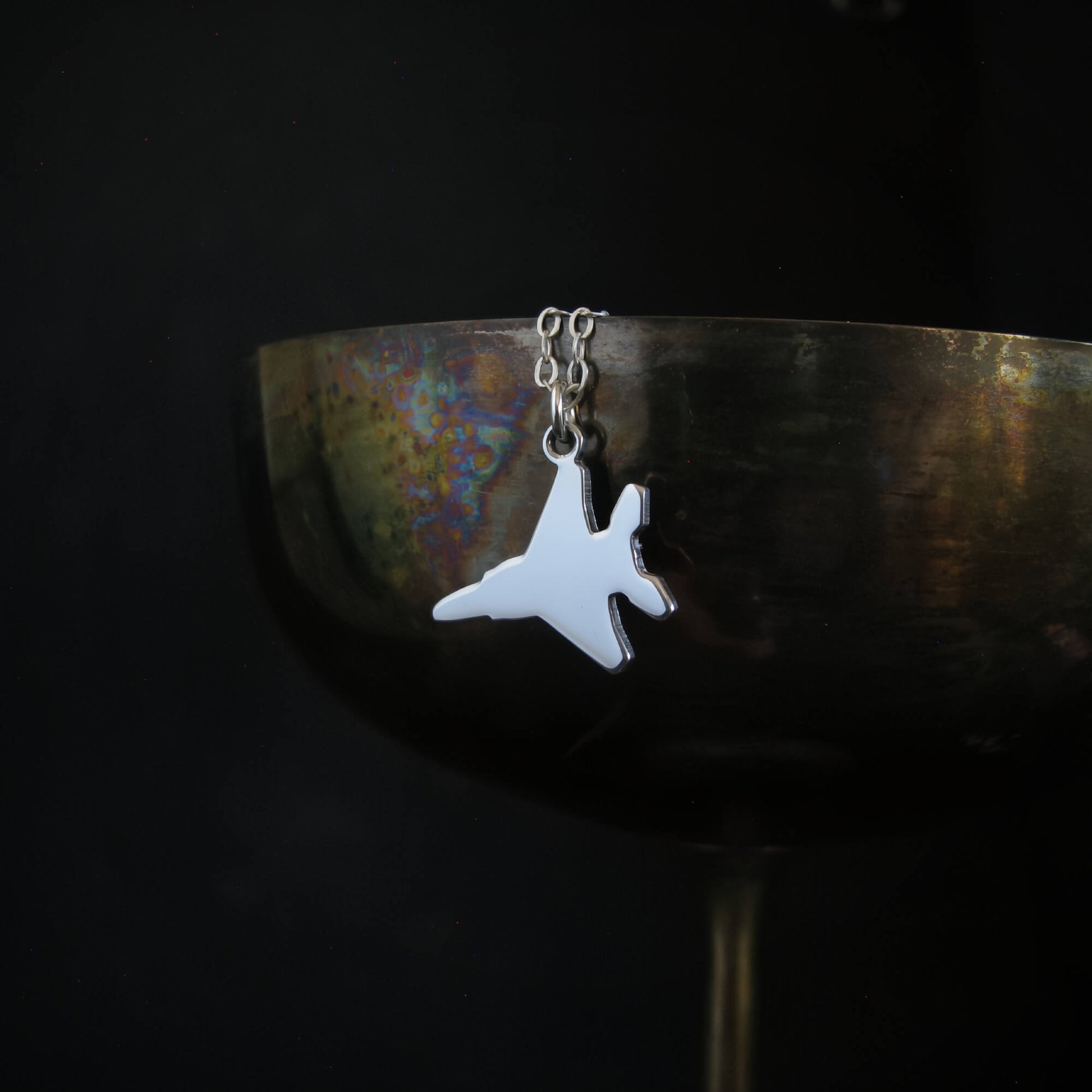 Polished sterling silver F-15 Eagle jet necklace hanging over oxidized silver goblet
