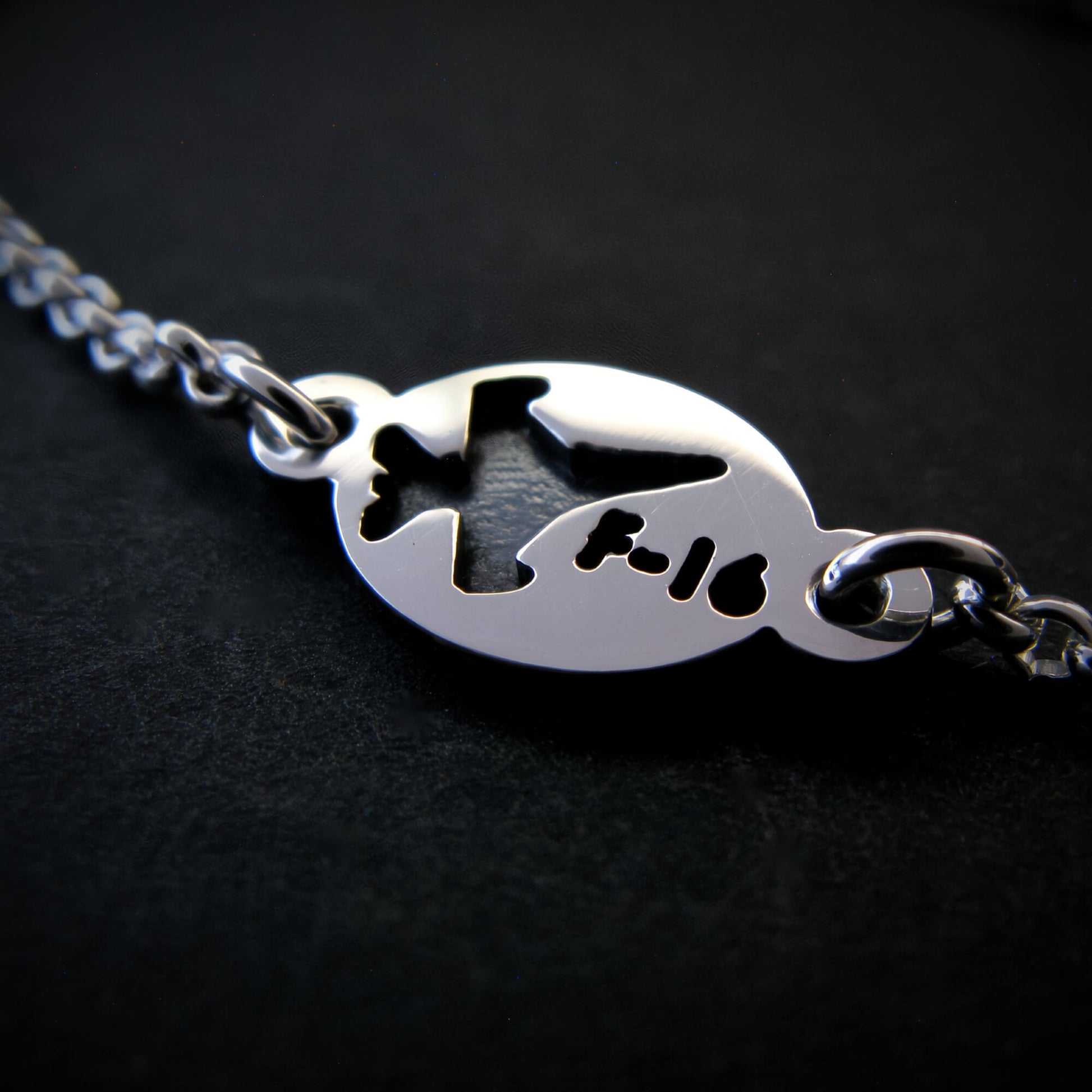 Silver bracelet with a round tag featuring an F-16 military fighter jet on a black background