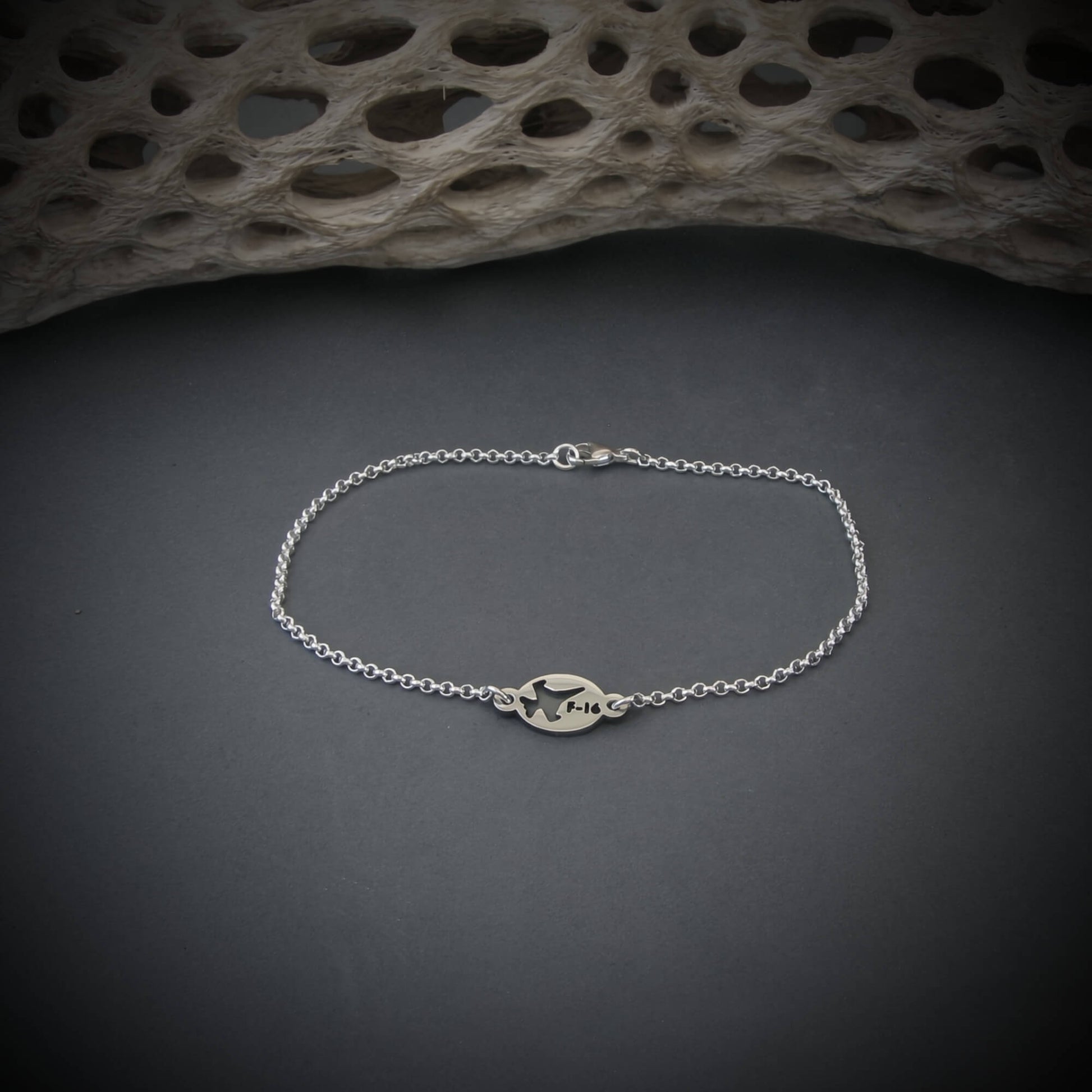 Silver bracelet with a round tag featuring an F-16 military fighter jet on a gray background