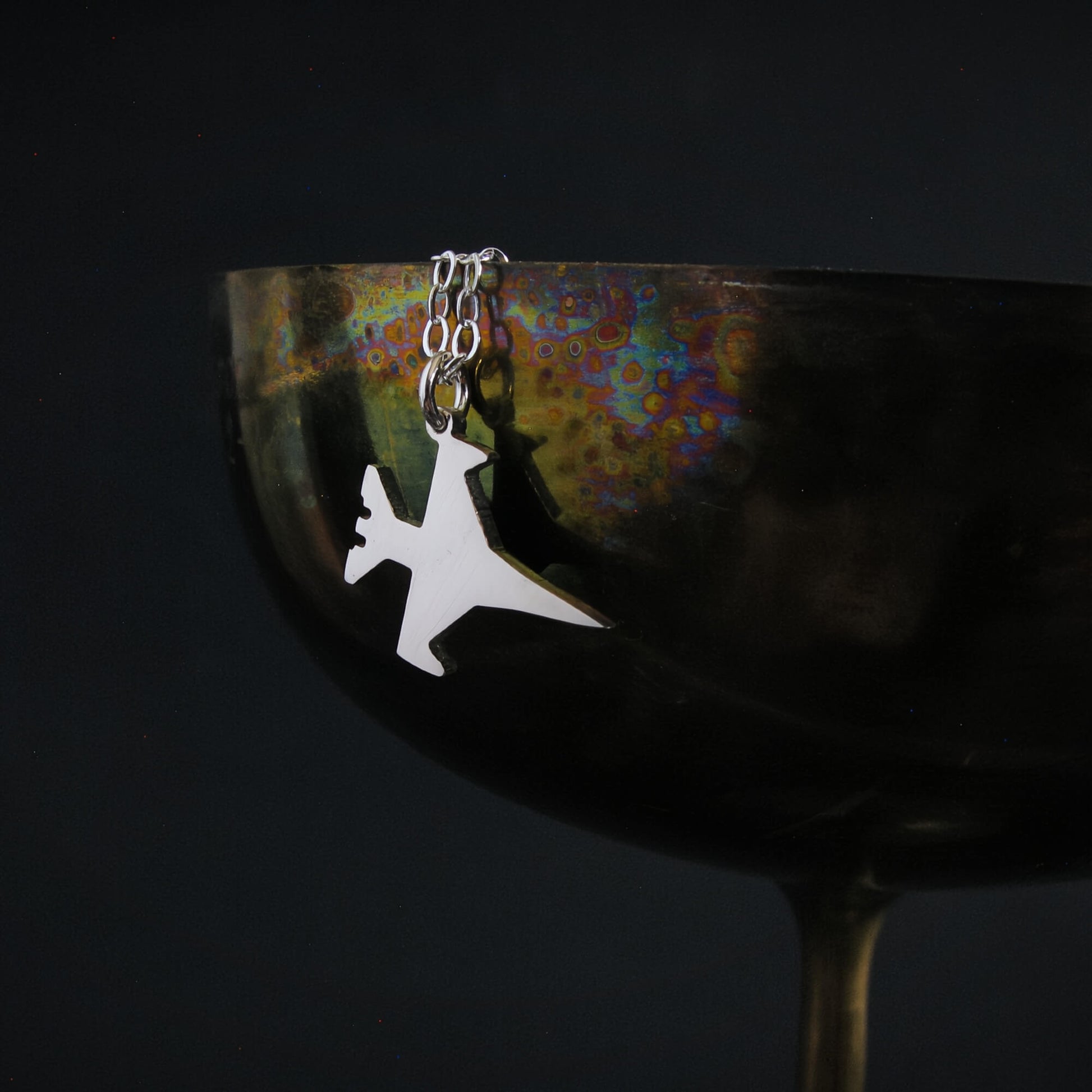 F-16 Viper jet pendant necklace draped over metallic bowl
