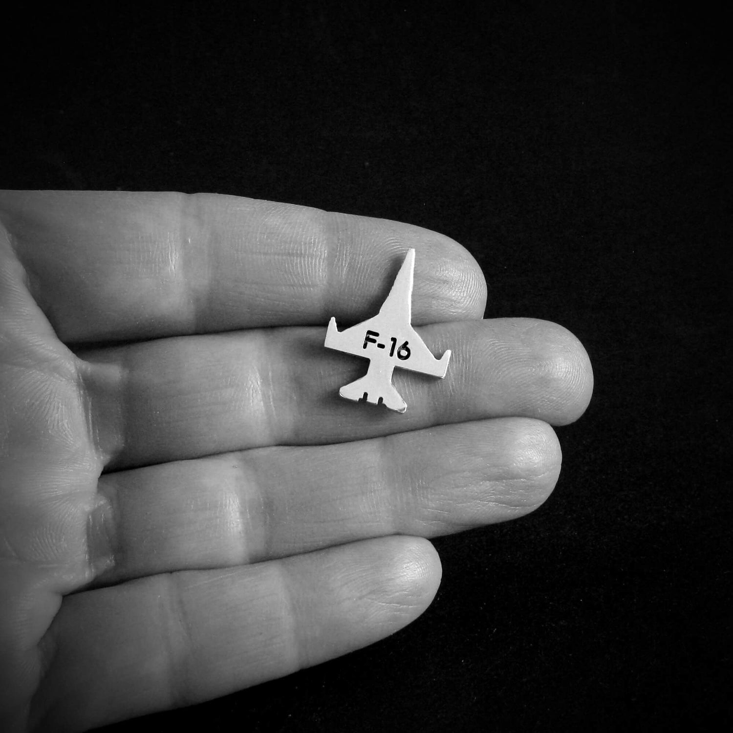 Small F-16 Viper military jet tie tack airplane held in a hand against a black background