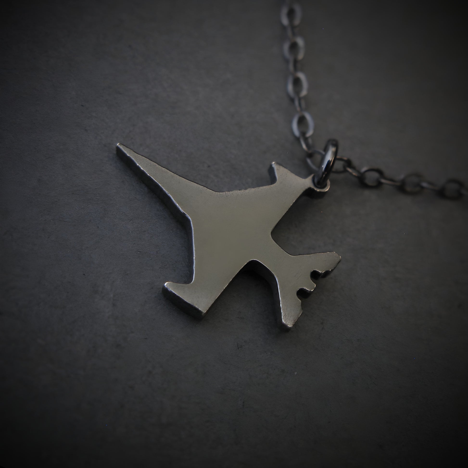 Dark sterling silver F-16 jet airplane-shaped pendant on a chain against a dark background