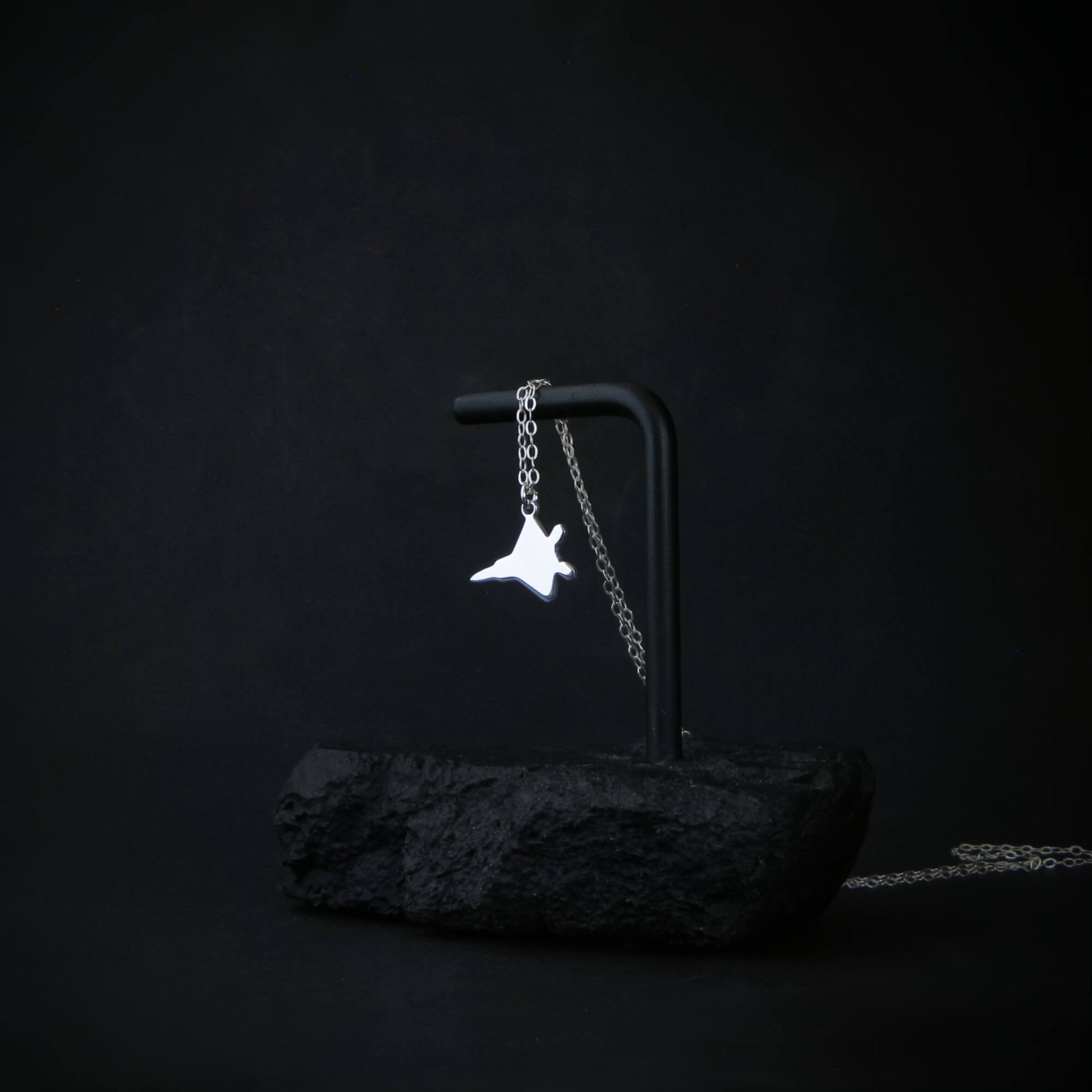 Sterling silver F-22 Raptor necklace draped on a black display with dark minimalist background