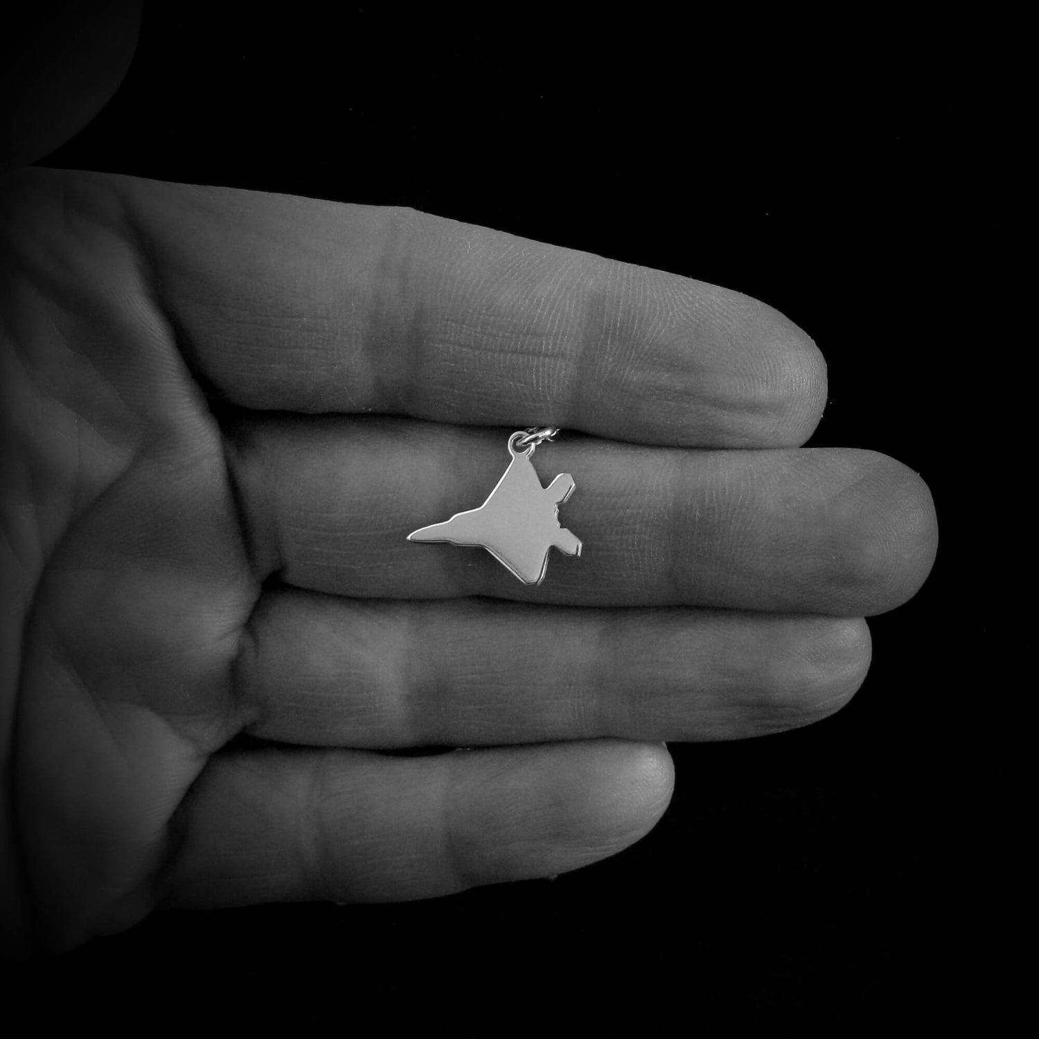 Sterling silver F-22 Raptor necklace draped on a hand with dark background