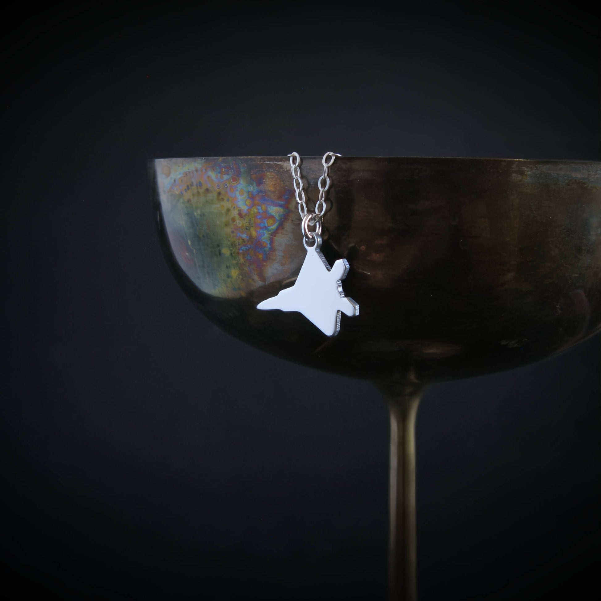 F-22 Raptor pendant in sterling silver hanging on the rim of a bronze cocktail glass