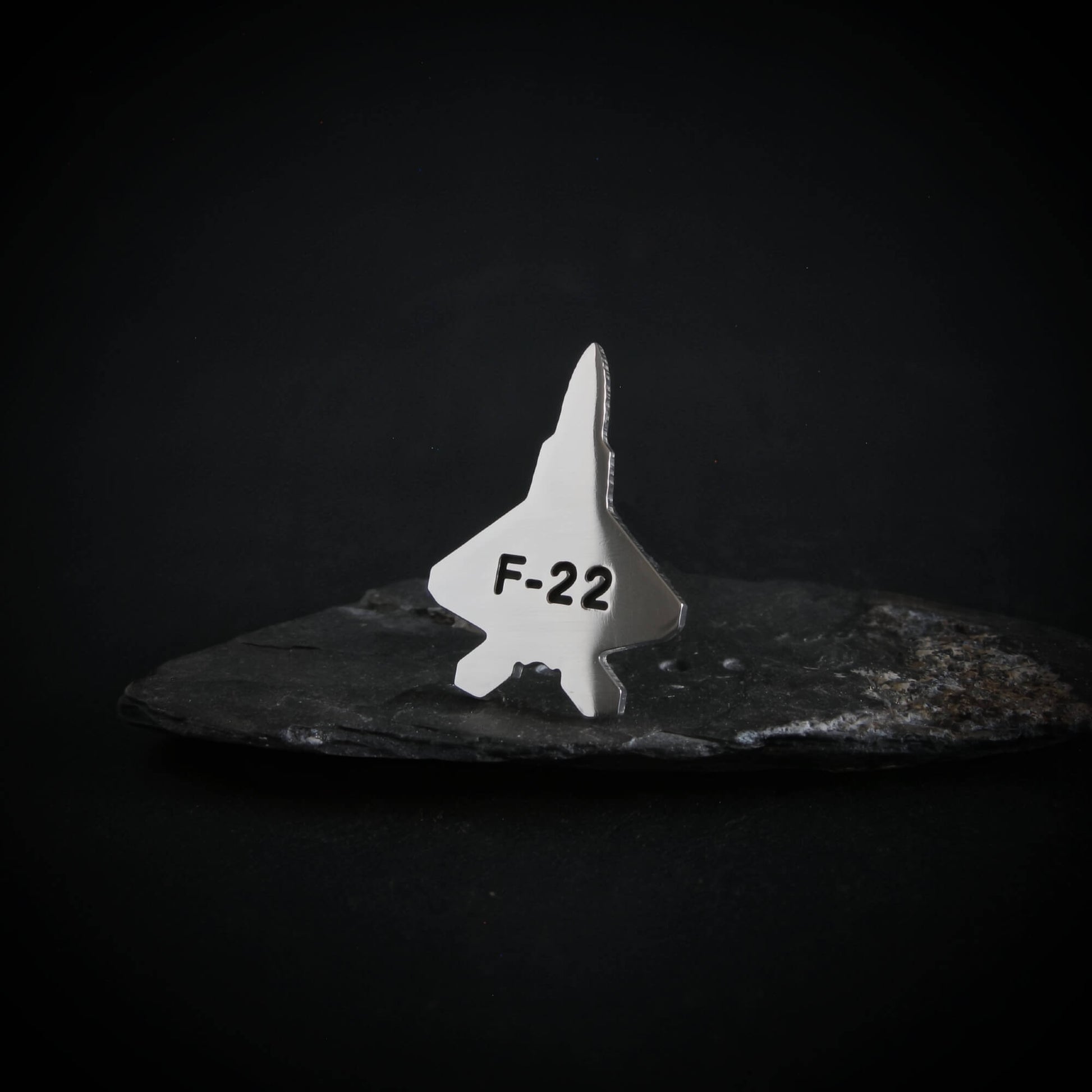 Silver F-22 fighter jet engraved tie pin on a dark background