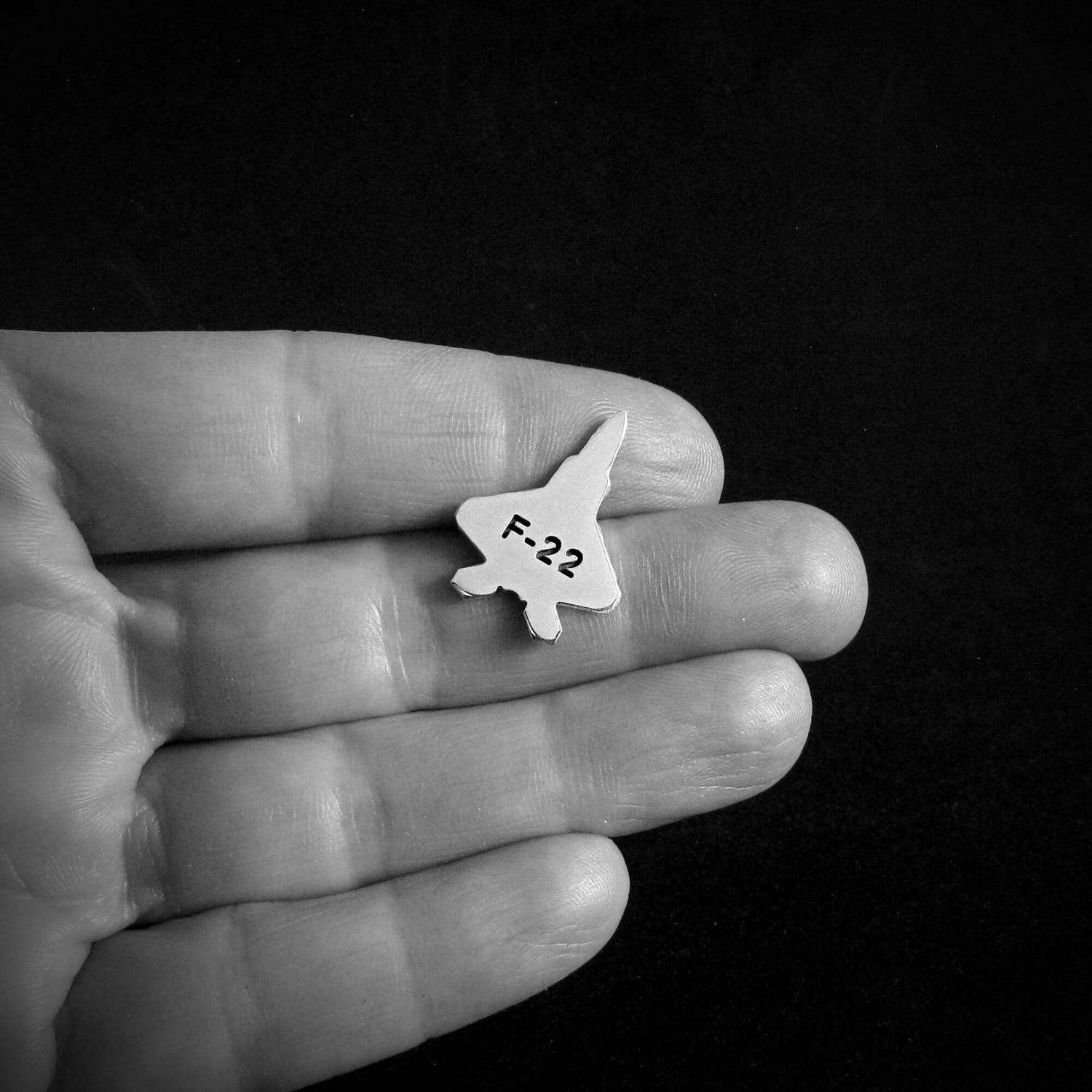 Small F-22 fighter jet airplane tie tack held in a hand against a black background