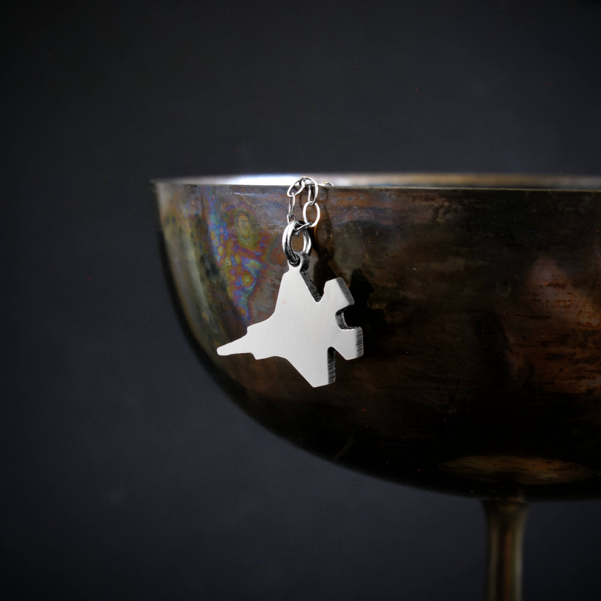 Sterling Silver F-35 Military Fighter Jet pendant on a chain hanging from a cup against a black background